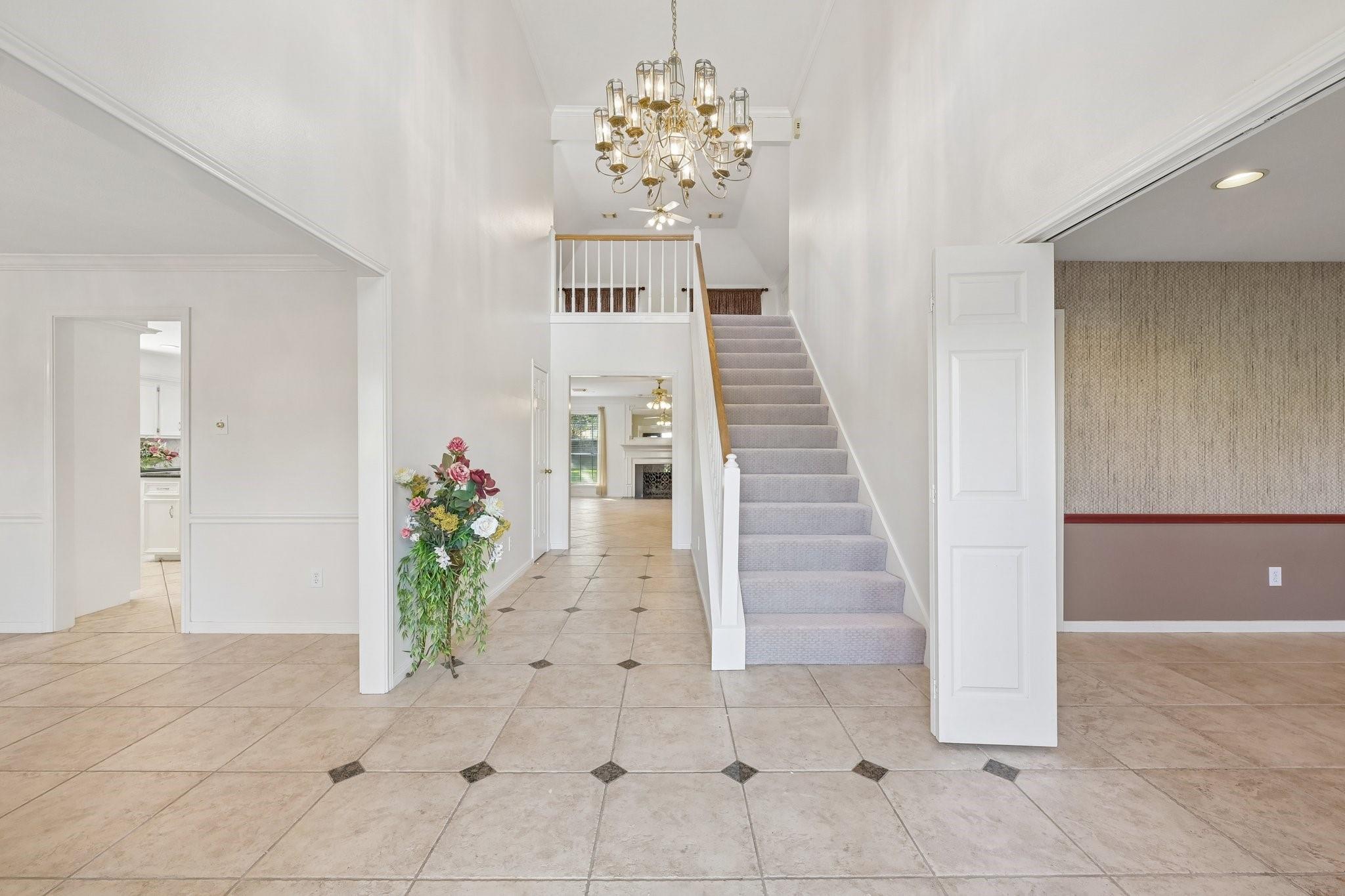 Entry hall with a tiled floor, carpeted staircase, and ornate chandelier.
