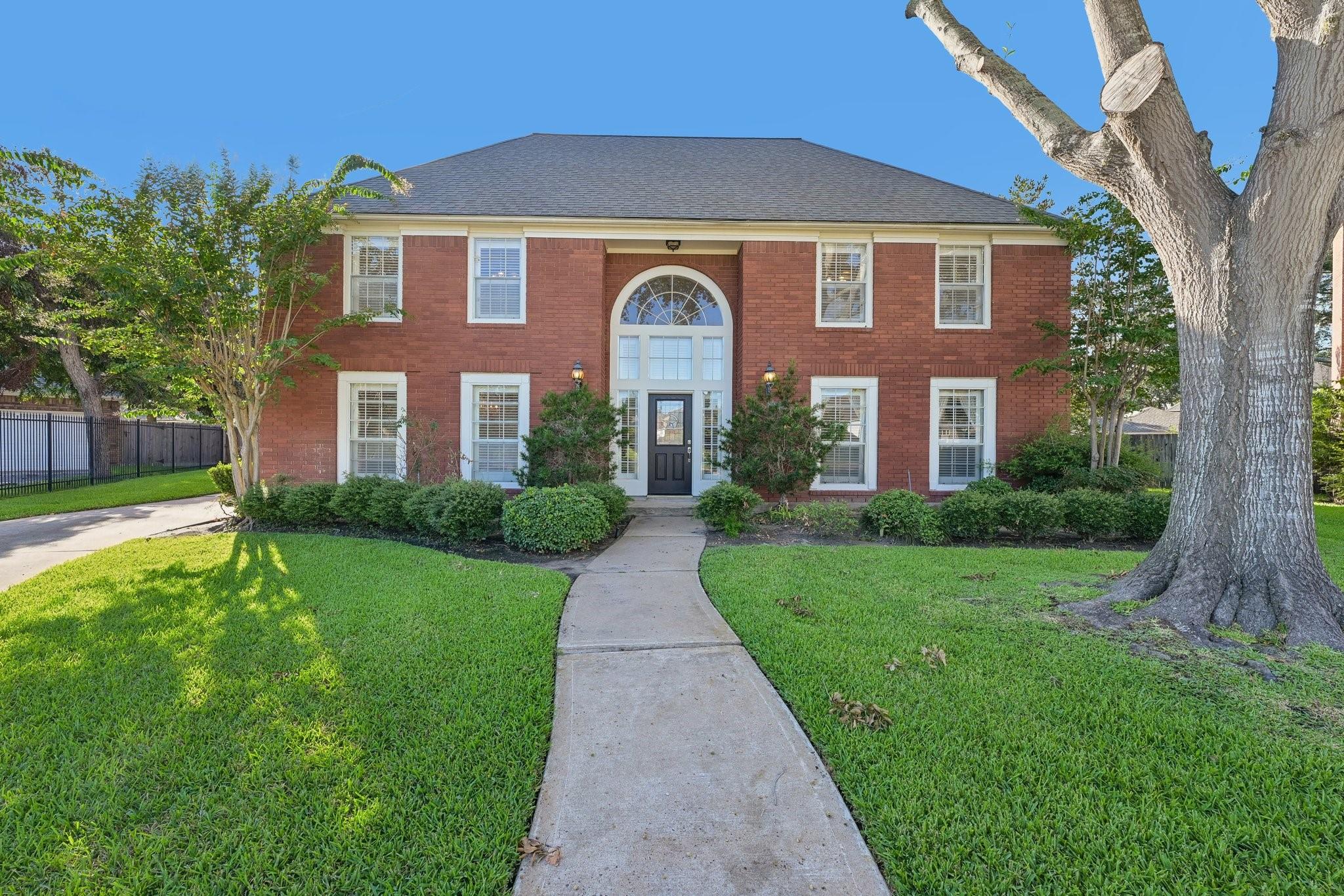 Two-story red brick house with an arched entry, front walkway, and large mature tree.