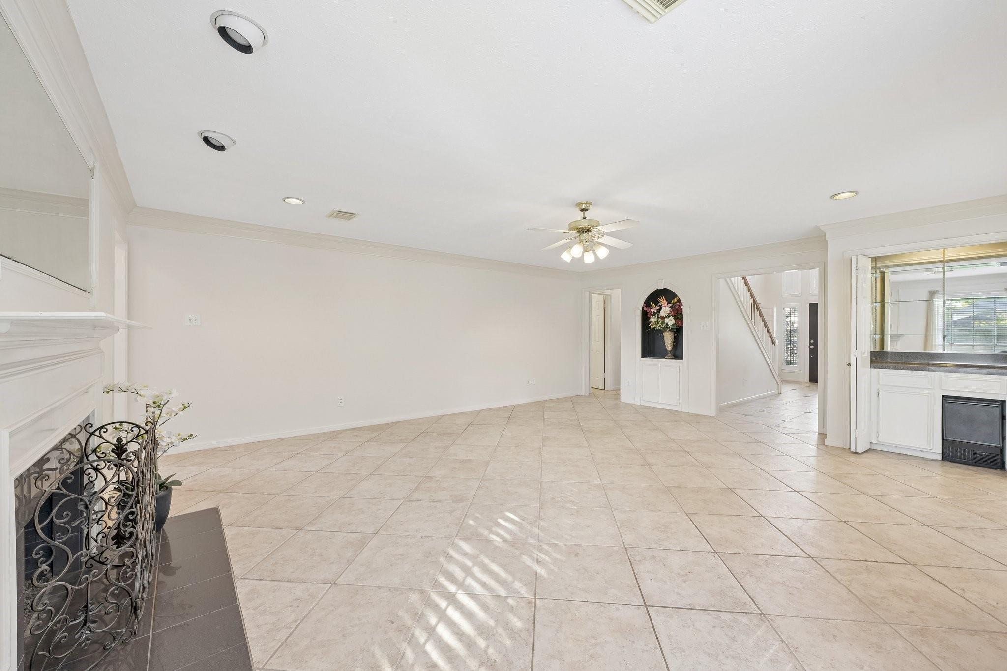 Mostly vacant living room with beige tile floors, a white fireplace, and a view toward the staircase.