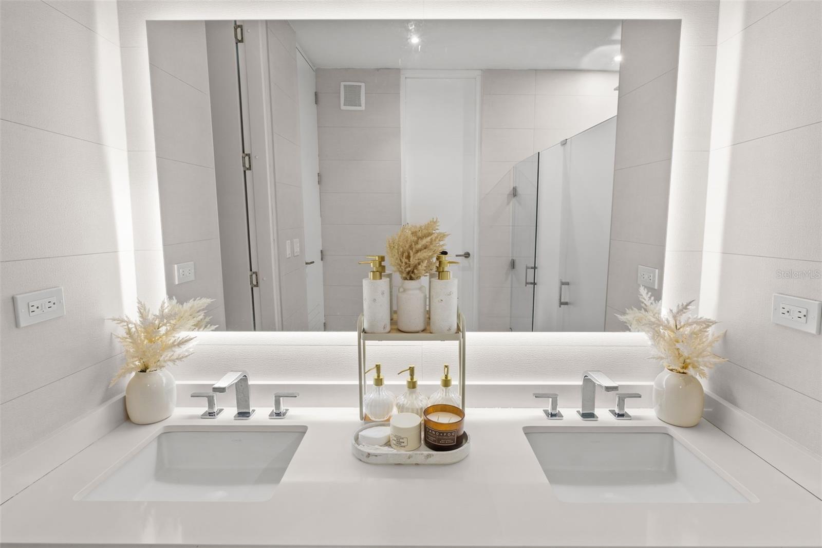 Modern bathroom with a double-sink vanity, illuminated mirror, and glass shower.