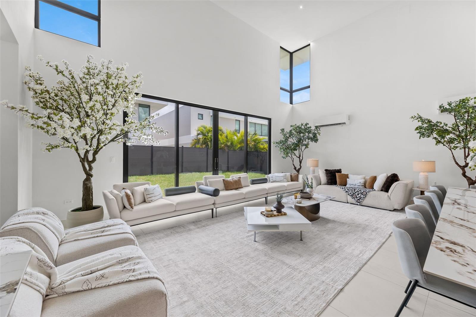 Living room with soaring ceilings, cream sofas, and large glass doors opening to a grassy courtyard.