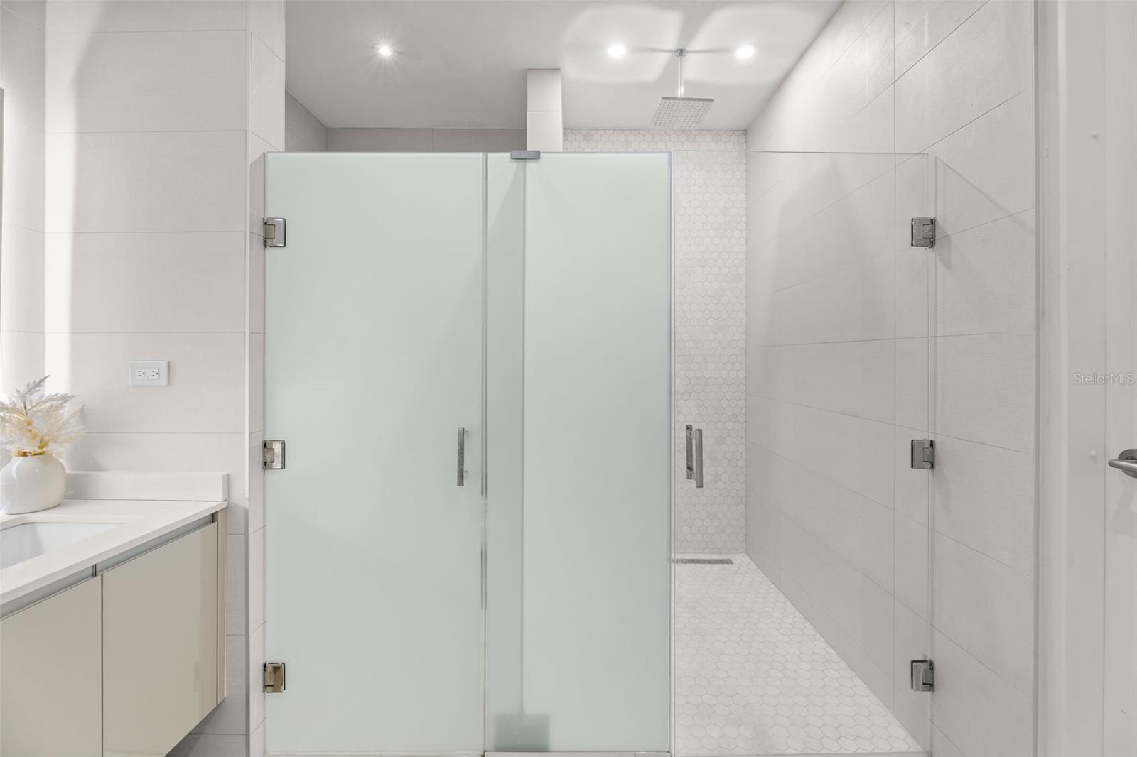 Modern bathroom with a spacious frosted-glass shower and white hexagonal tile.