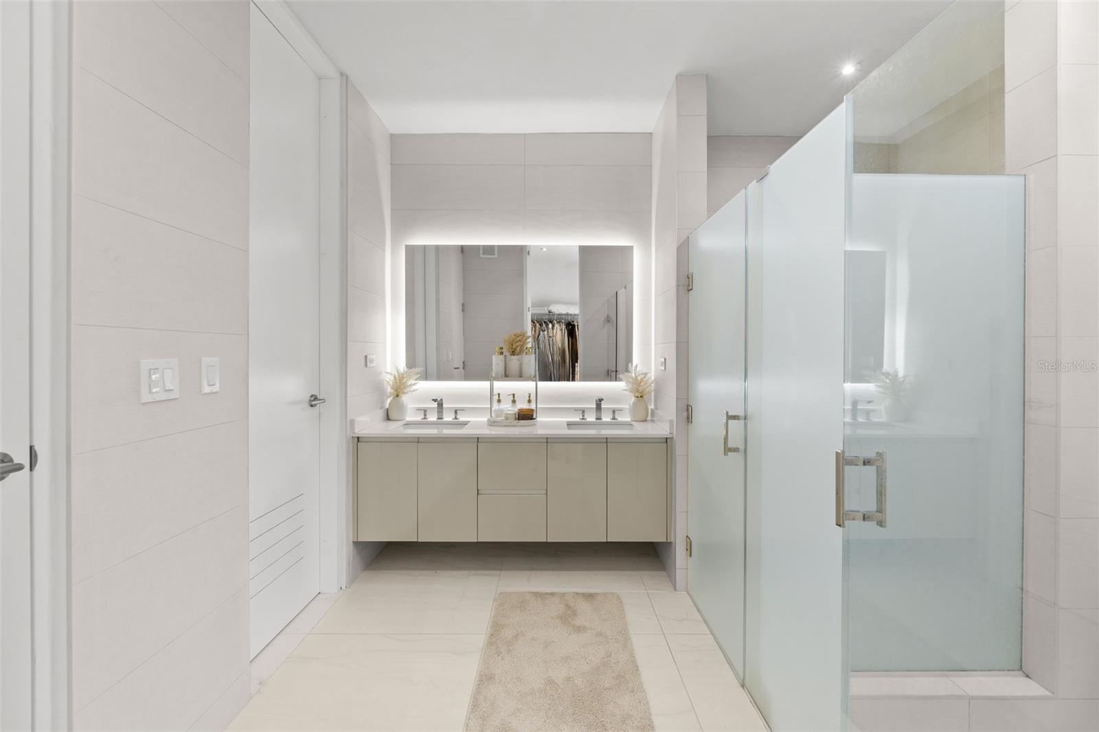 Modern bathroom with a double vanity, backlit mirror, and glass-enclosed shower.