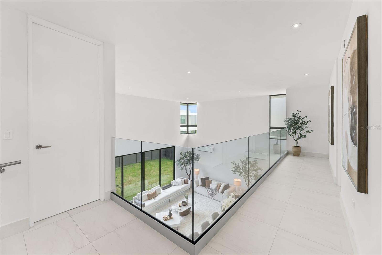 Modern upstairs hallway with glass railing overlooking a furnished living room