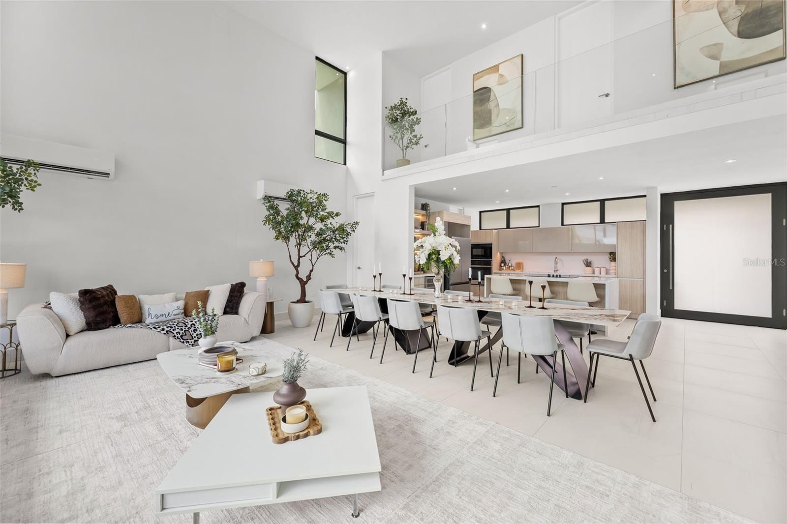 Double-height living and dining room with a white sectional, long table, and modern open kitchen.