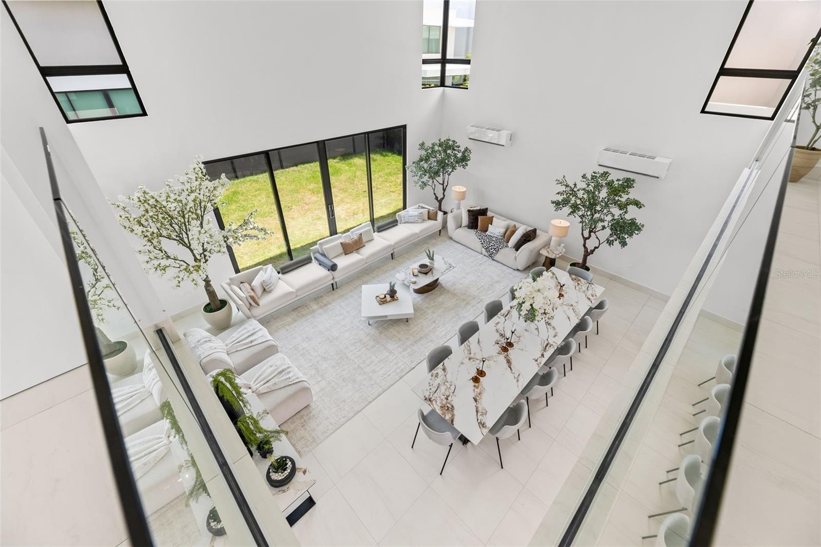 Open-plan living and dining room with double-height windows, white sofas, and a long dining table.