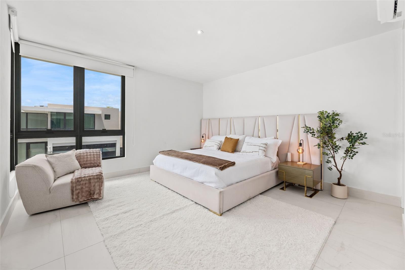 Staged bedroom with a blush upholstered bed and large black-framed window.