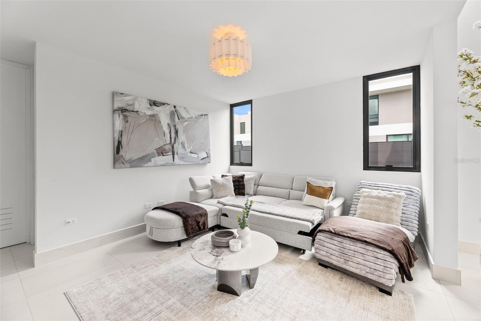 Bright living room with a gray sectional, chaise lounge, round coffee table, and abstract wall art.