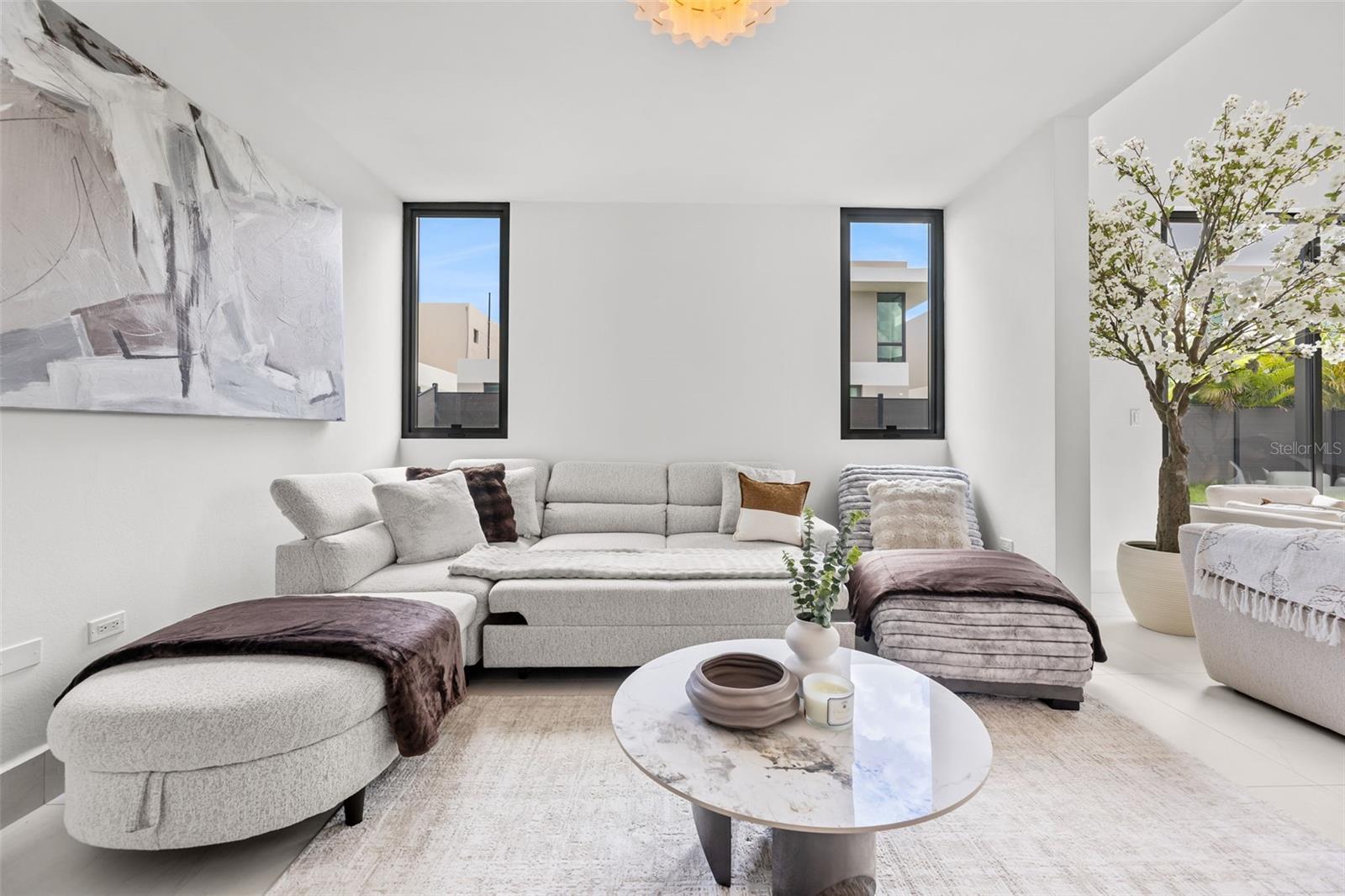Bright living room with a gray sectional, oval coffee table, abstract art, and tall windows.
