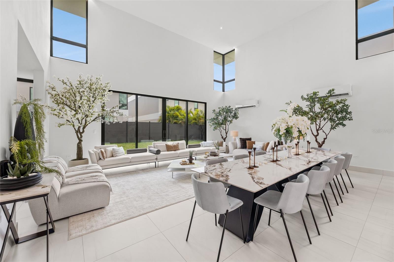 Open-plan living and dining room with a marble table, white sofas, and tall courtyard-facing windows.