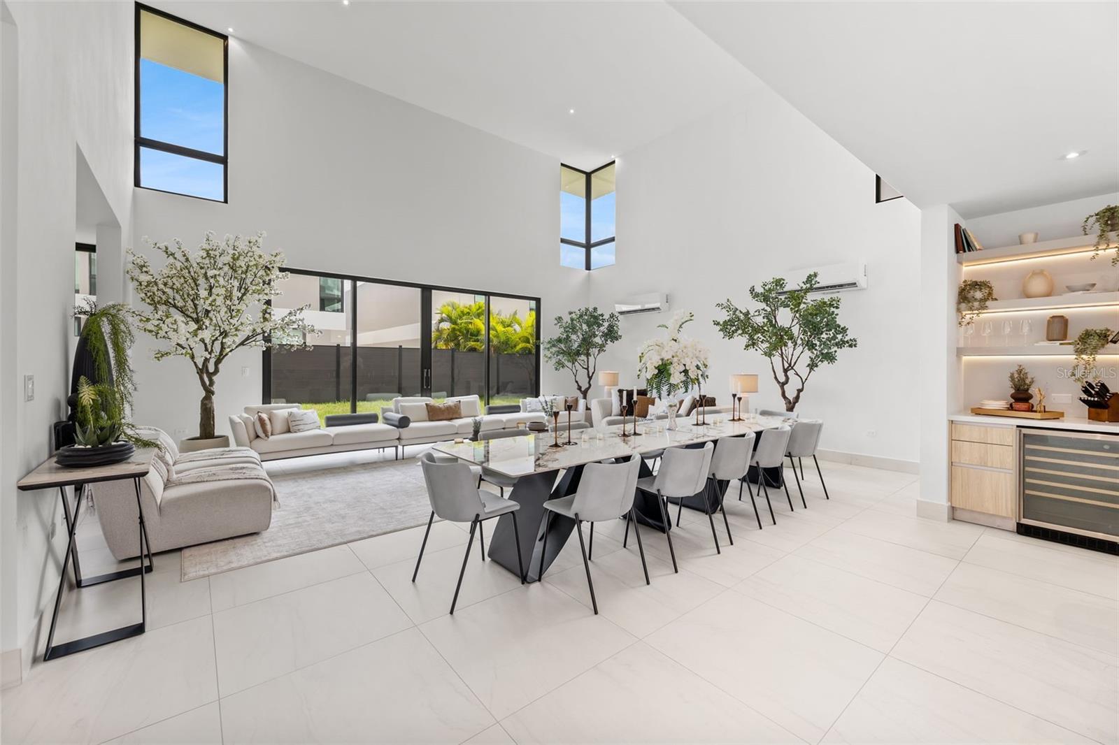 Open-plan living and dining room with a long table, pale sofas, and tall windows.