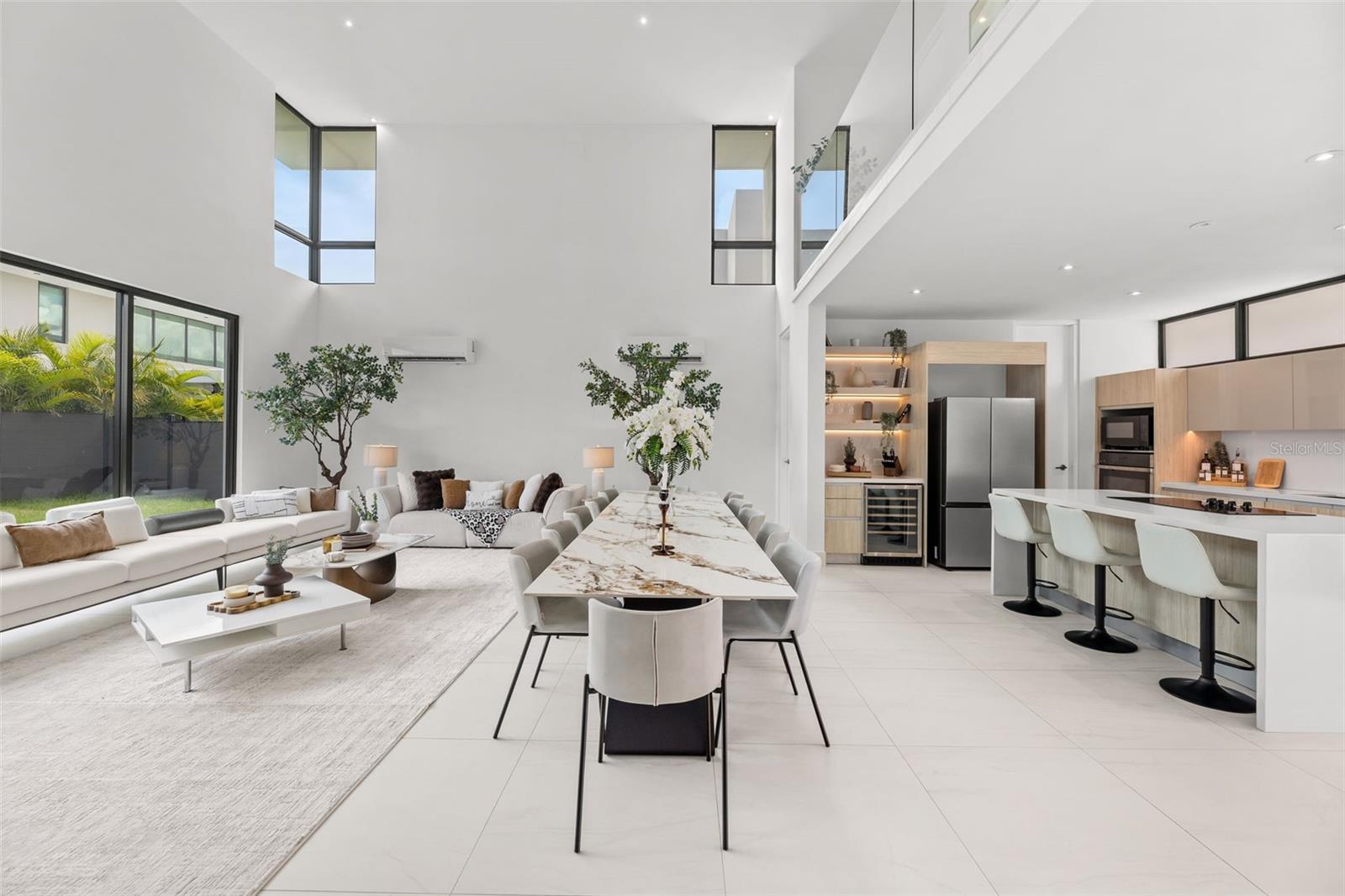 Open-plan living, dining, and kitchen area with a double-height ceiling, large windows, and marble dining table.