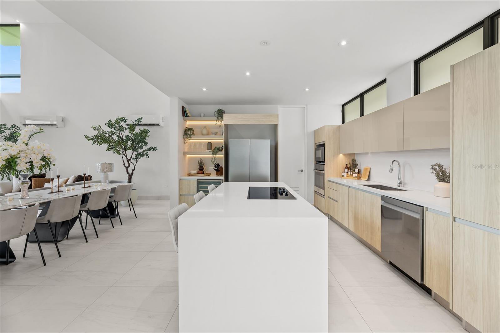 Modern open-plan kitchen with a large white island, pale wood cabinetry, and adjoining dining area.