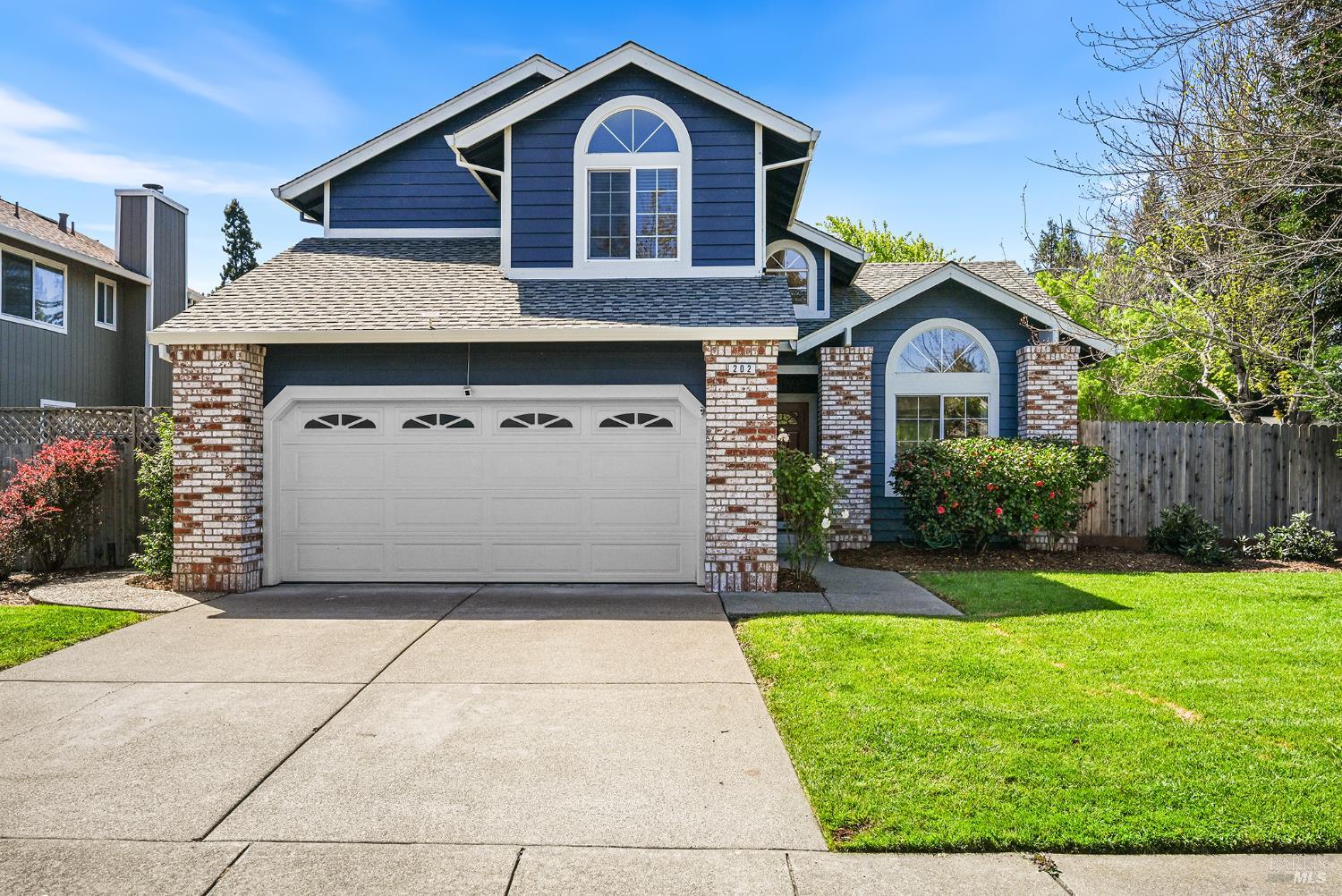 Blue two-story home with arched windows, brick columns, and a double garage.