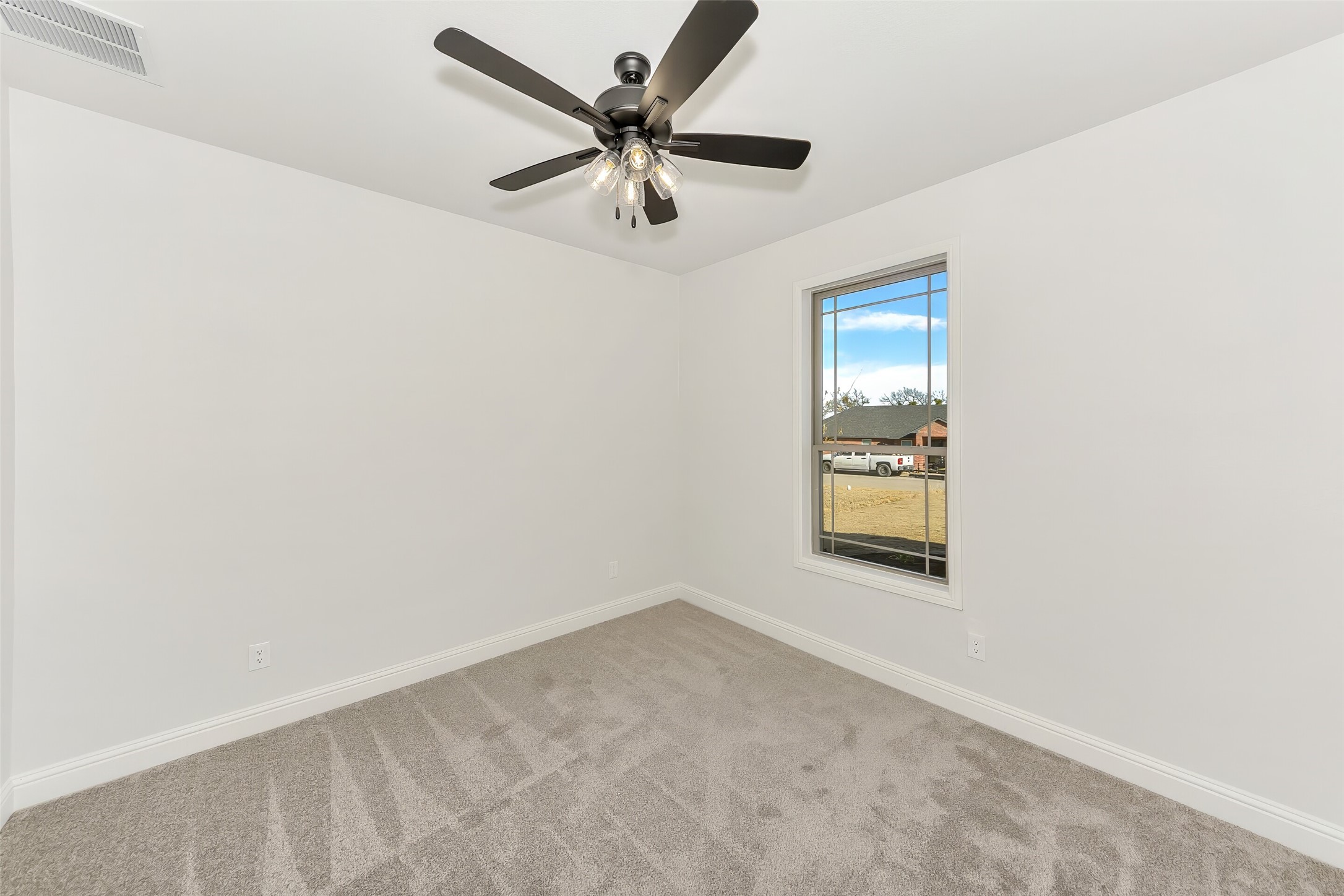 Empty carpeted bedroom with a ceiling fan and single window.