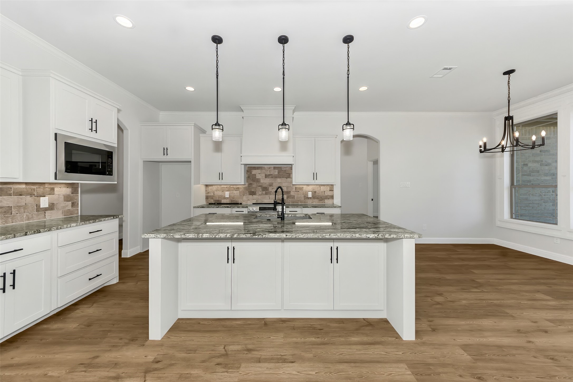 Bright kitchen with white cabinetry, a large granite island, and pendant lights.