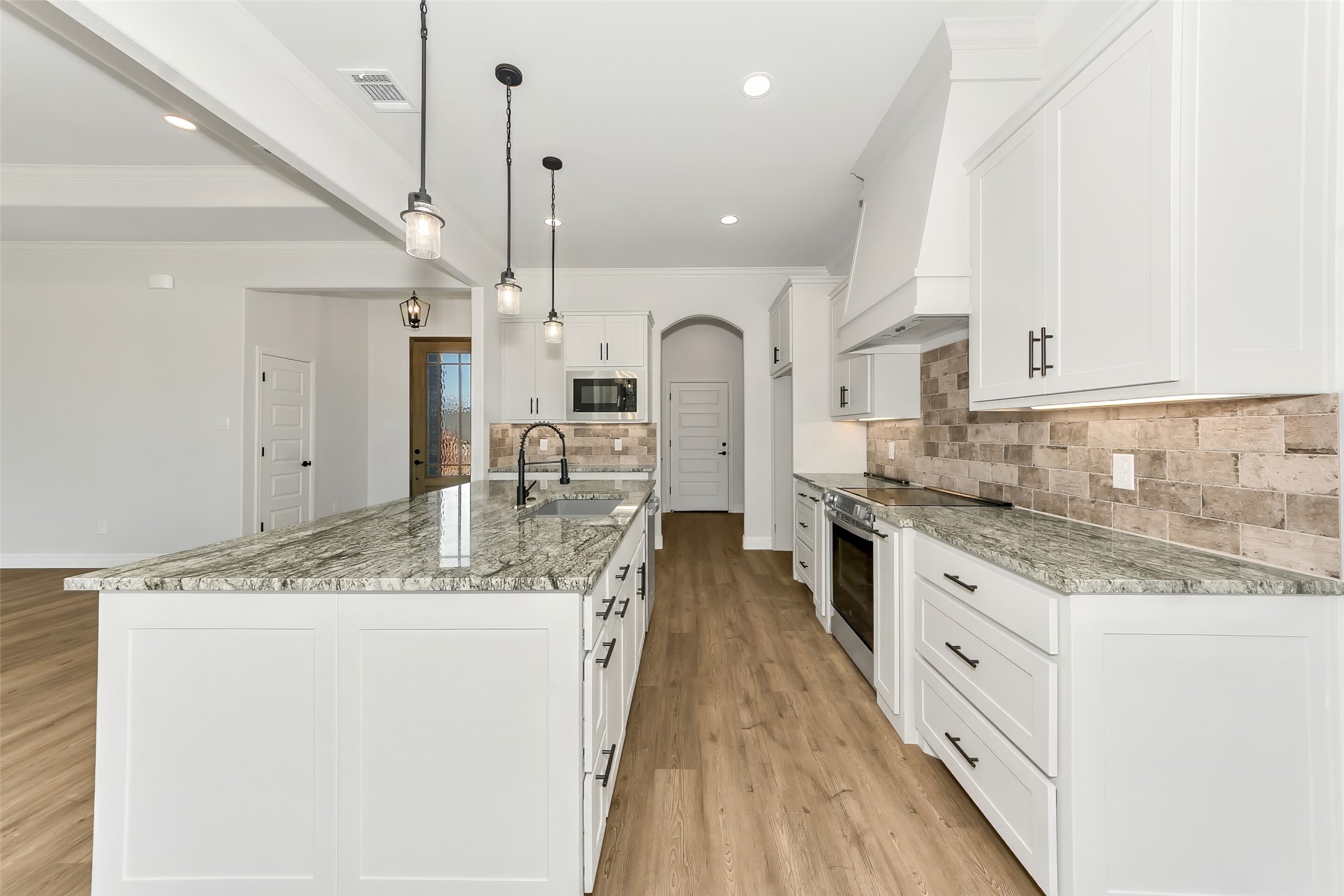 Bright kitchen with a large granite island, white cabinets, and a stone tile backsplash.