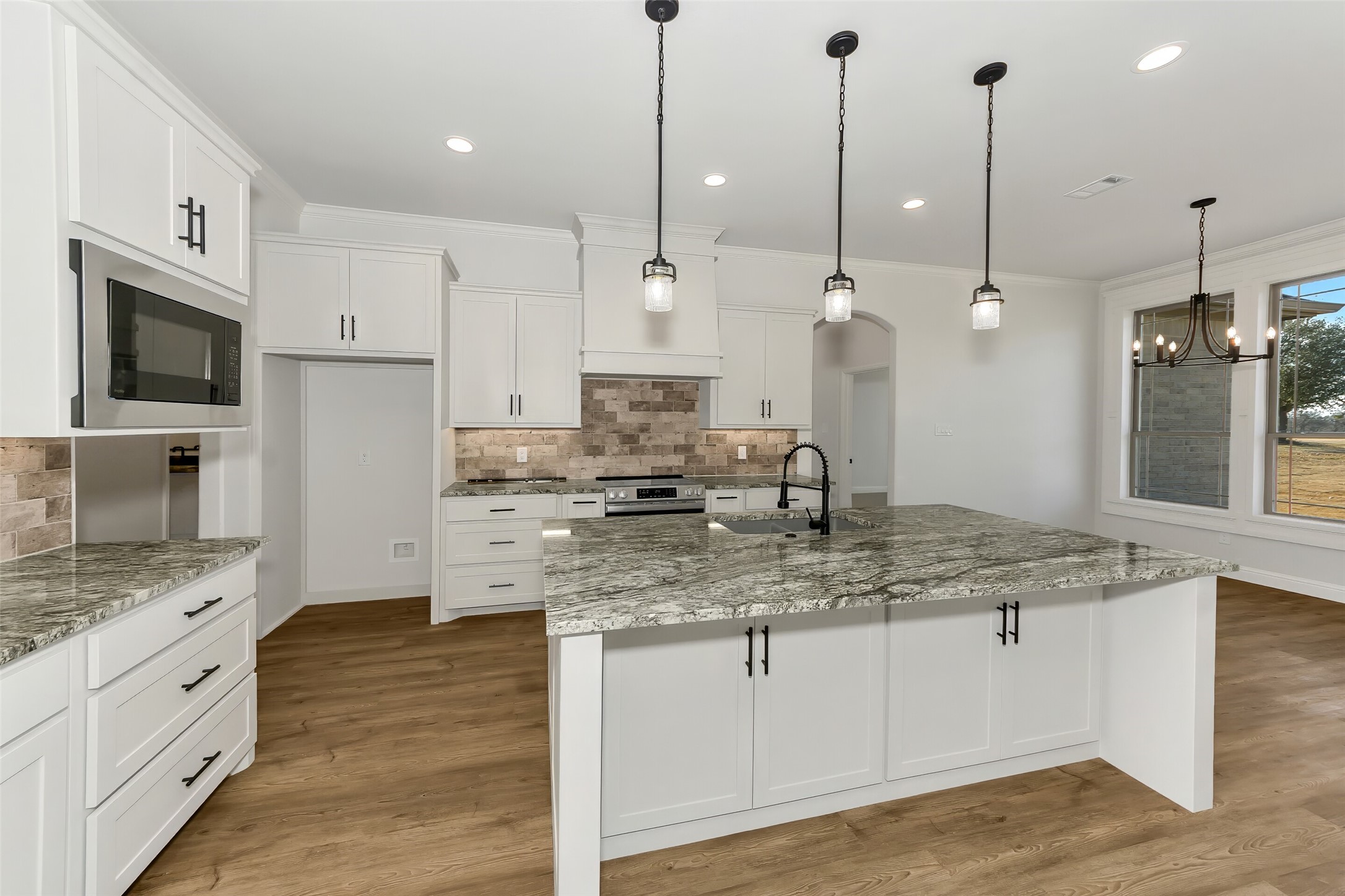 Bright kitchen with white cabinets, a large granite island, and pendant lights.