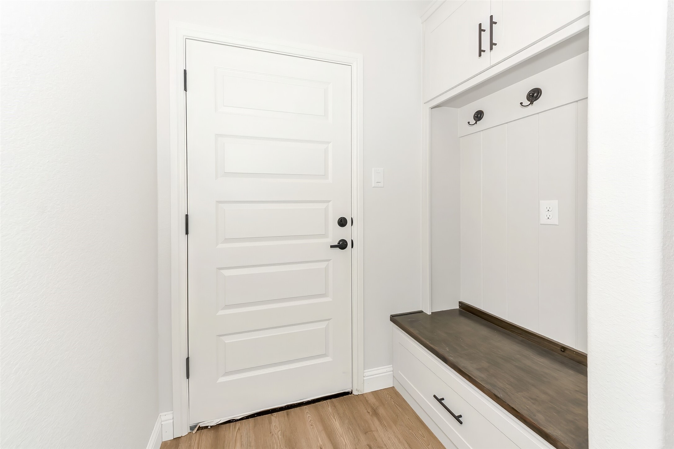 Entryway with a white paneled front door and built-in bench, hooks, and cabinets.