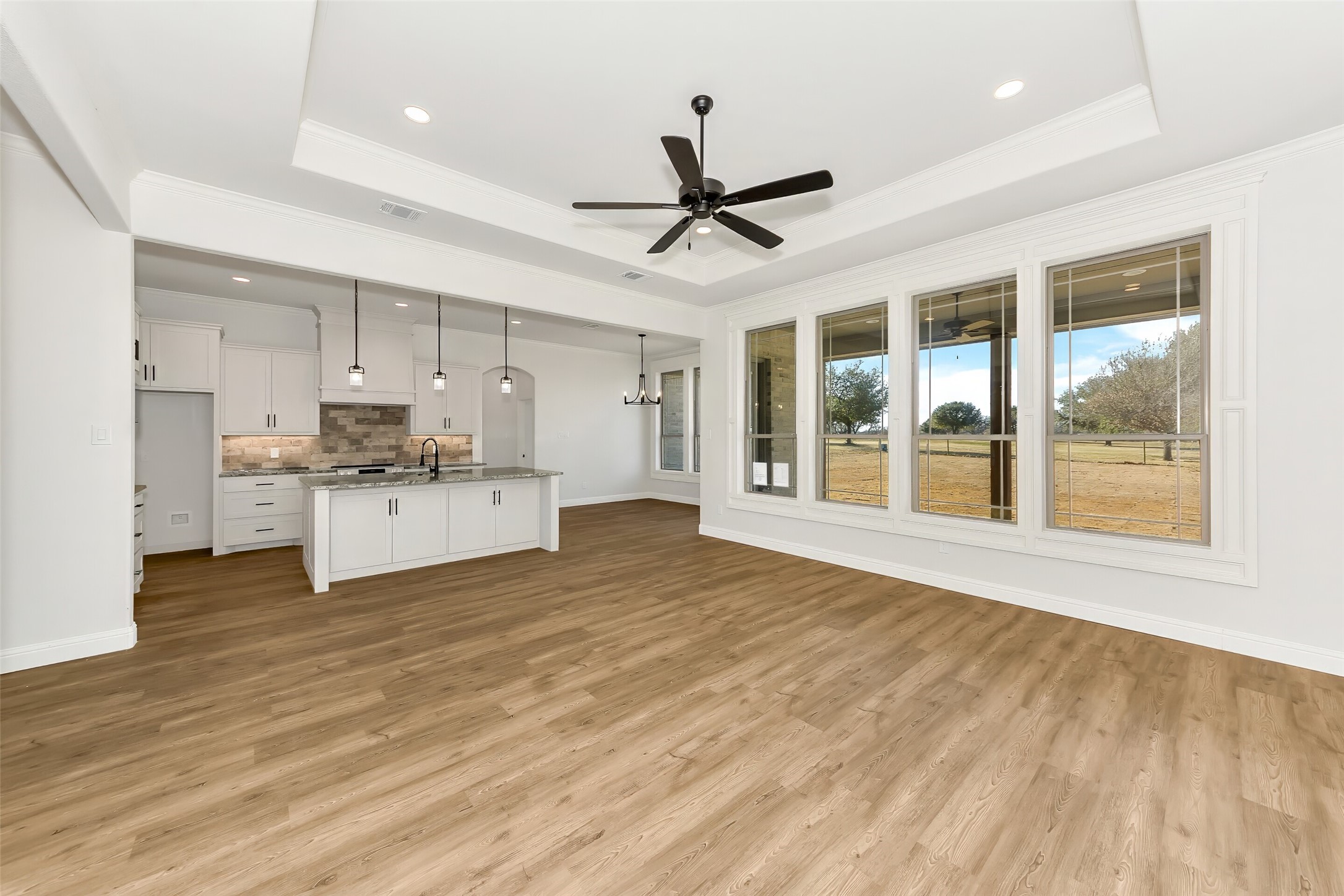 Open kitchen and living area with a white island, wood floors, and large windows overlooking the yard.