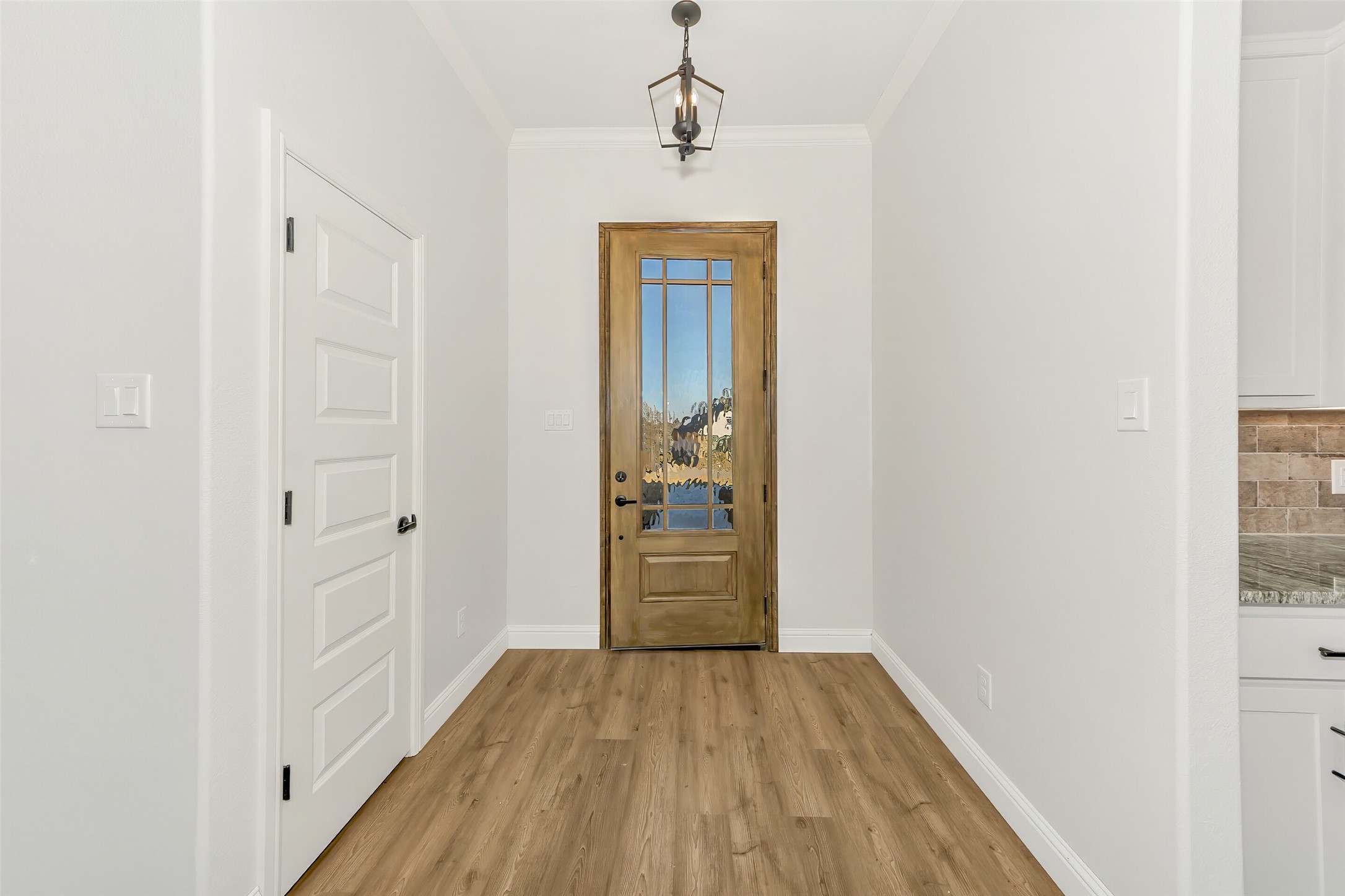 Entry foyer with a wood-and-glass front door, wood flooring, and a hanging light fixture.