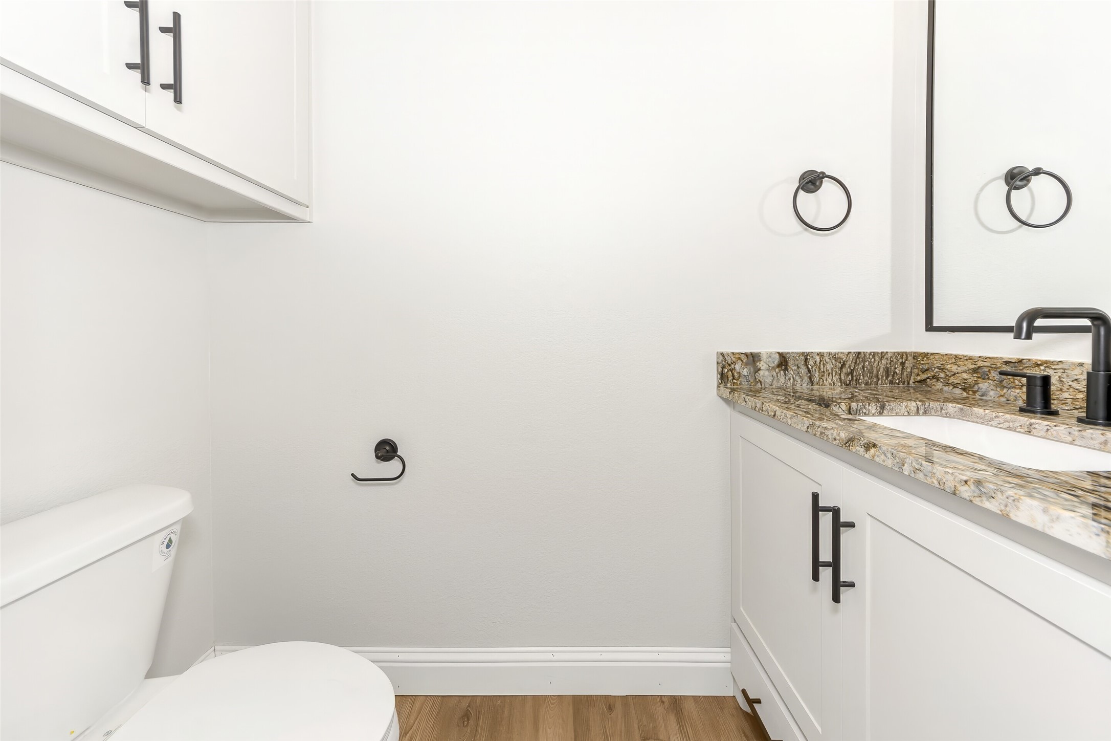 Bathroom with white cabinetry, a granite vanity, black fixtures, and a toilet.