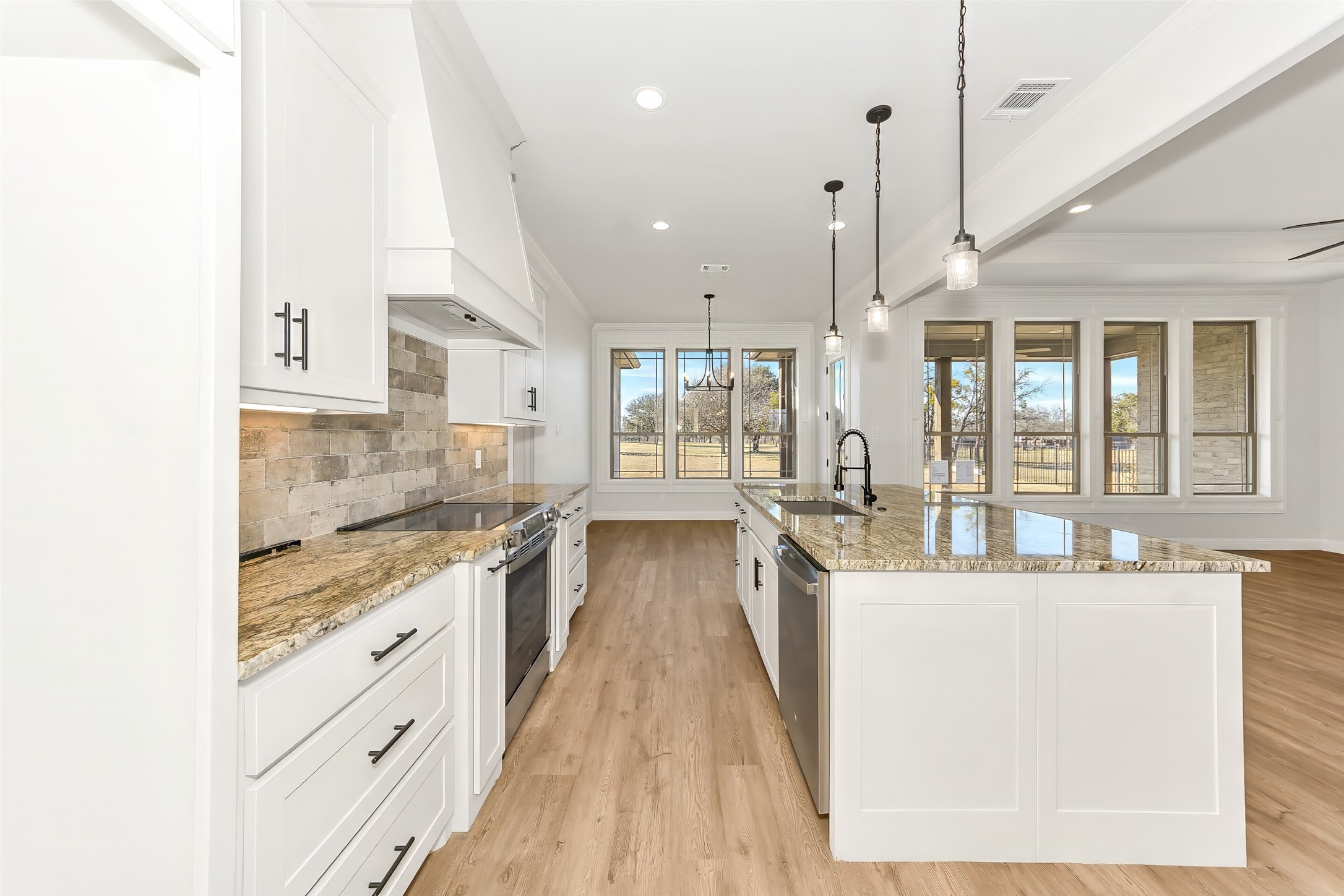 Bright kitchen with a large granite island, white cabinetry, and tall windows overlooking the yard.