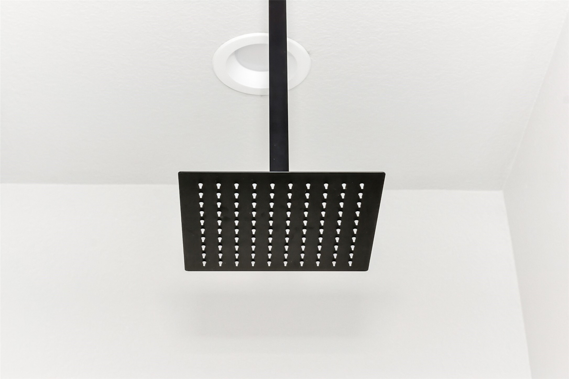 Matte black square rainfall showerhead mounted against white shower walls.