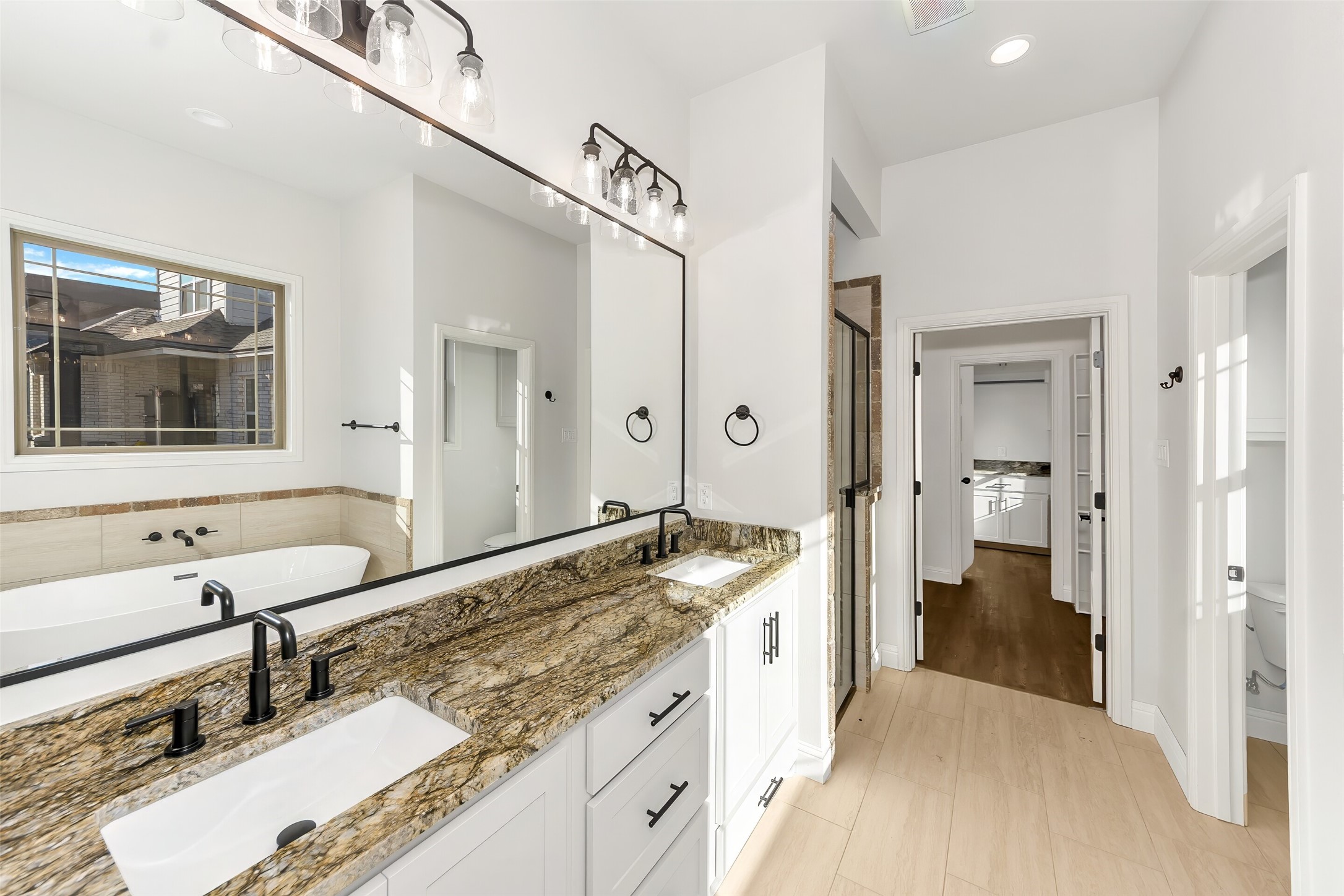 Bright bathroom with a double vanity, patterned stone countertop, and freestanding bathtub.