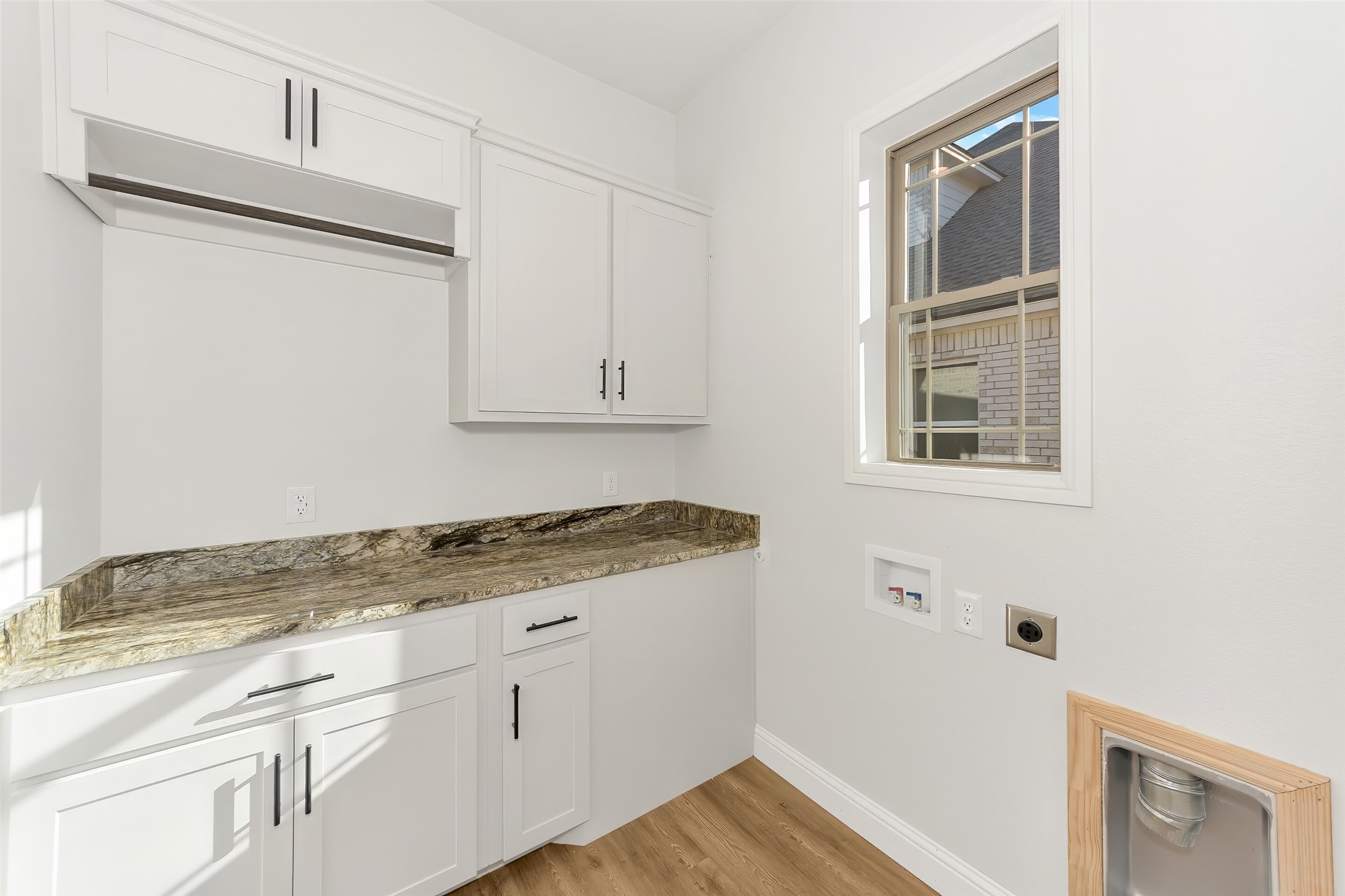 Laundry room with white cabinets, stone countertop, washer hookups, and a window.