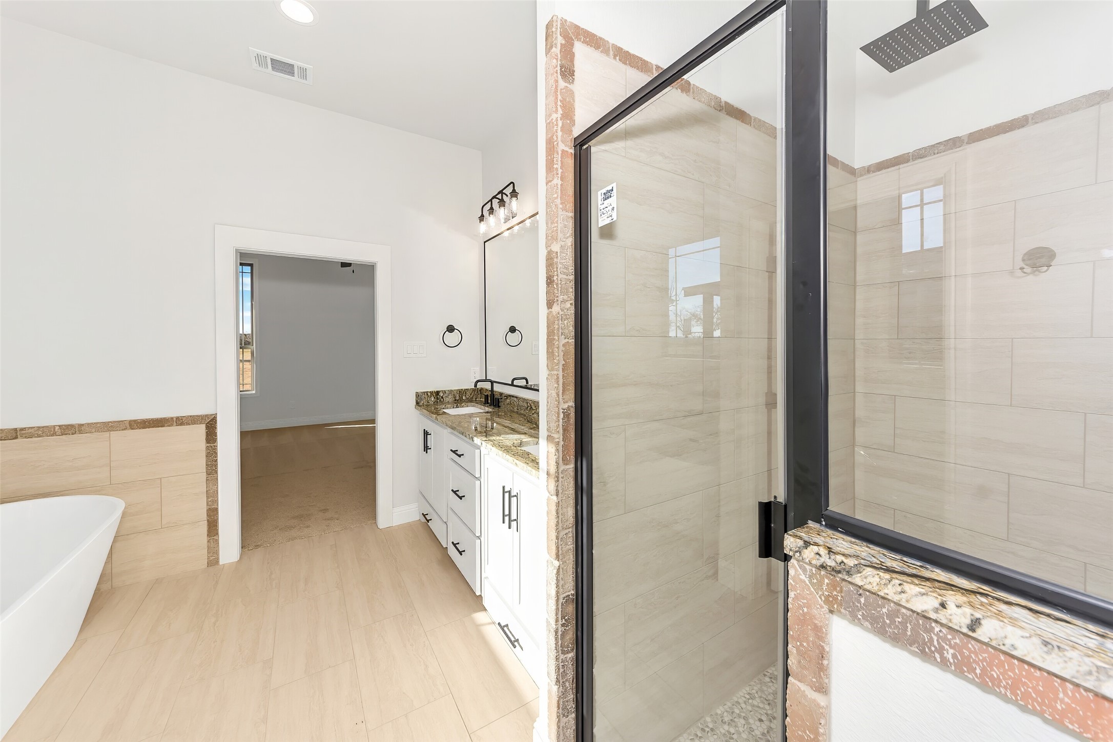 Bathroom with a glass-enclosed tiled shower, freestanding tub, and granite vanity.