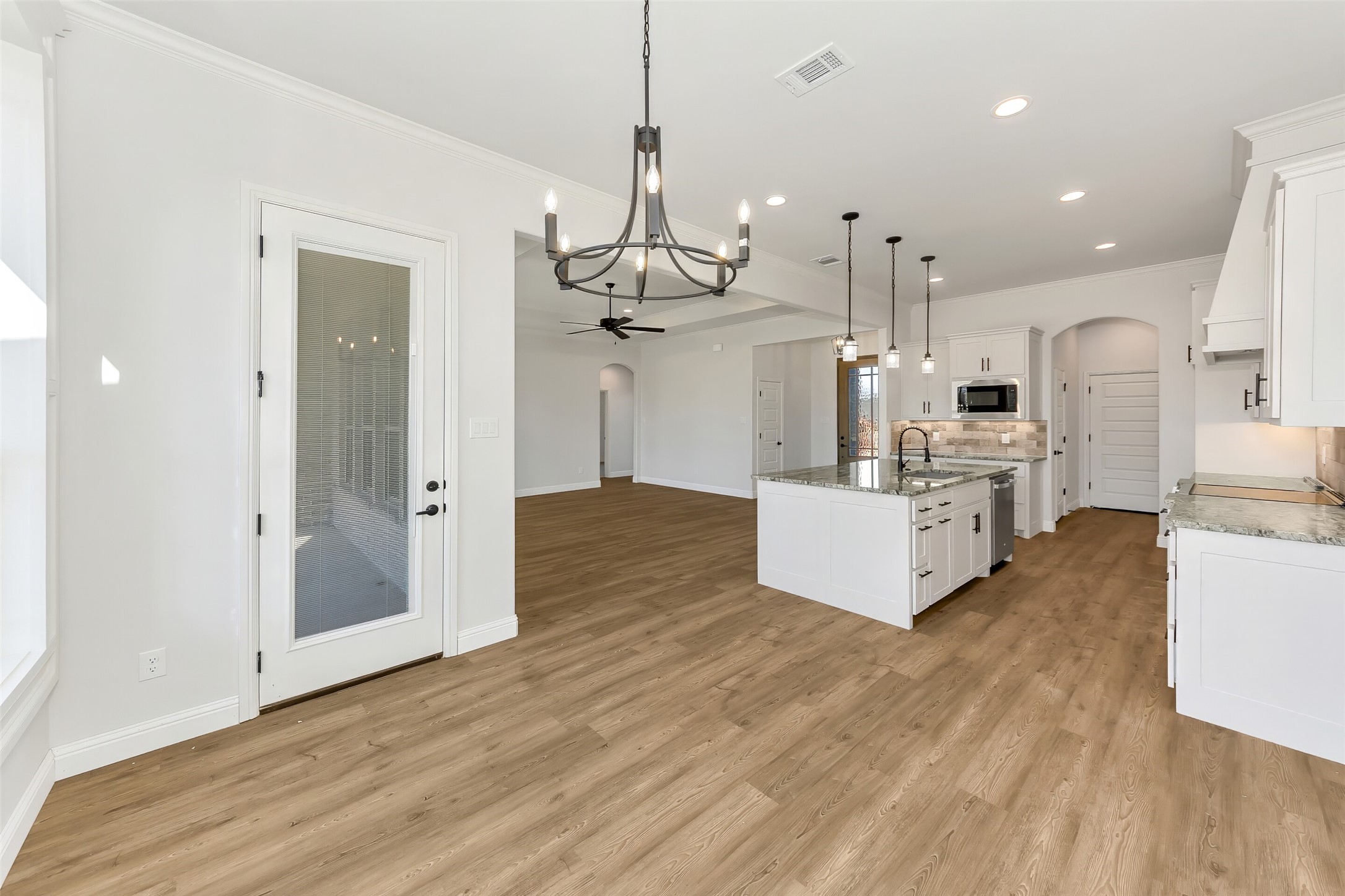 Open kitchen with a large island, white cabinets, and warm wood flooring.