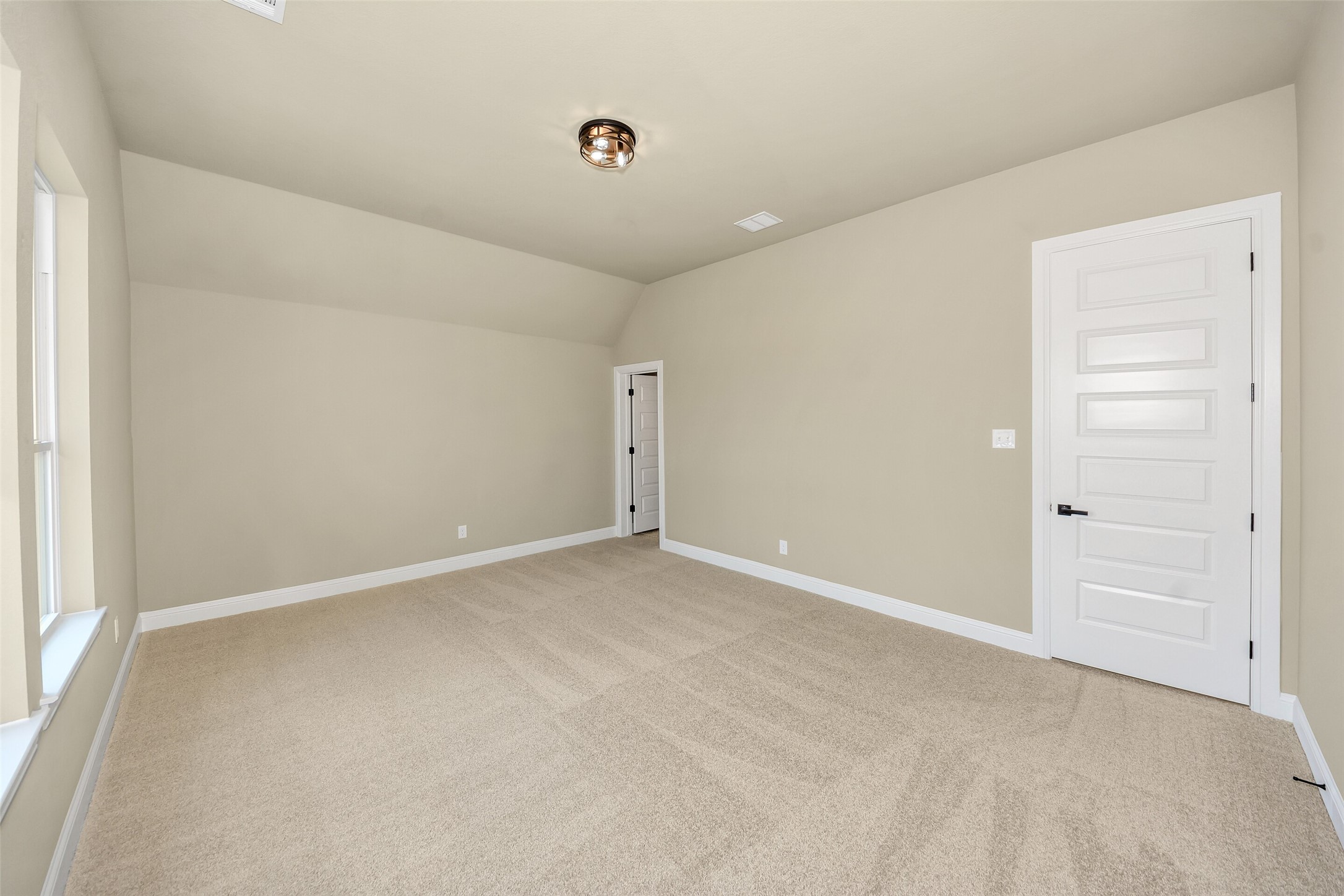 Empty carpeted room with beige walls, a tall window, and two white doors.
