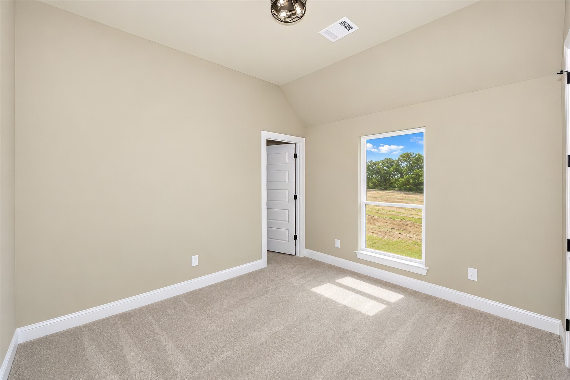 Empty carpeted room with beige walls and a tall window overlooking trees.