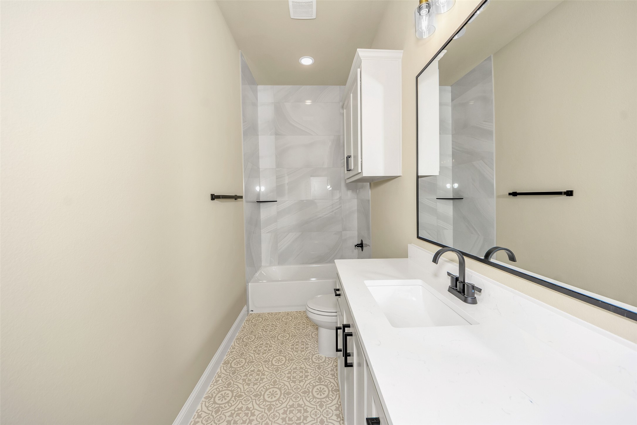 Bathroom with a white vanity, gray tiled tub surround, and patterned beige floor tiles.