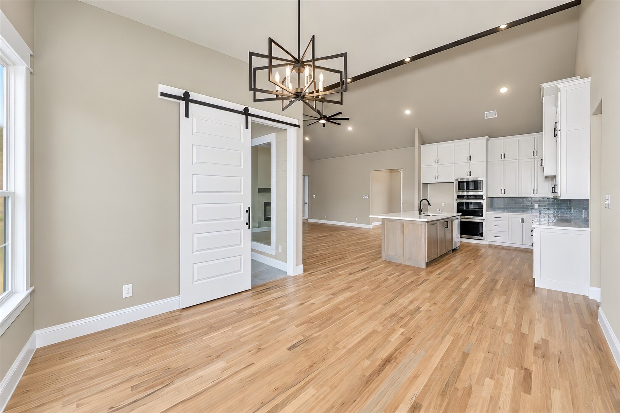 Open kitchen with white cabinets, central island, wood floors, and sliding barn door.