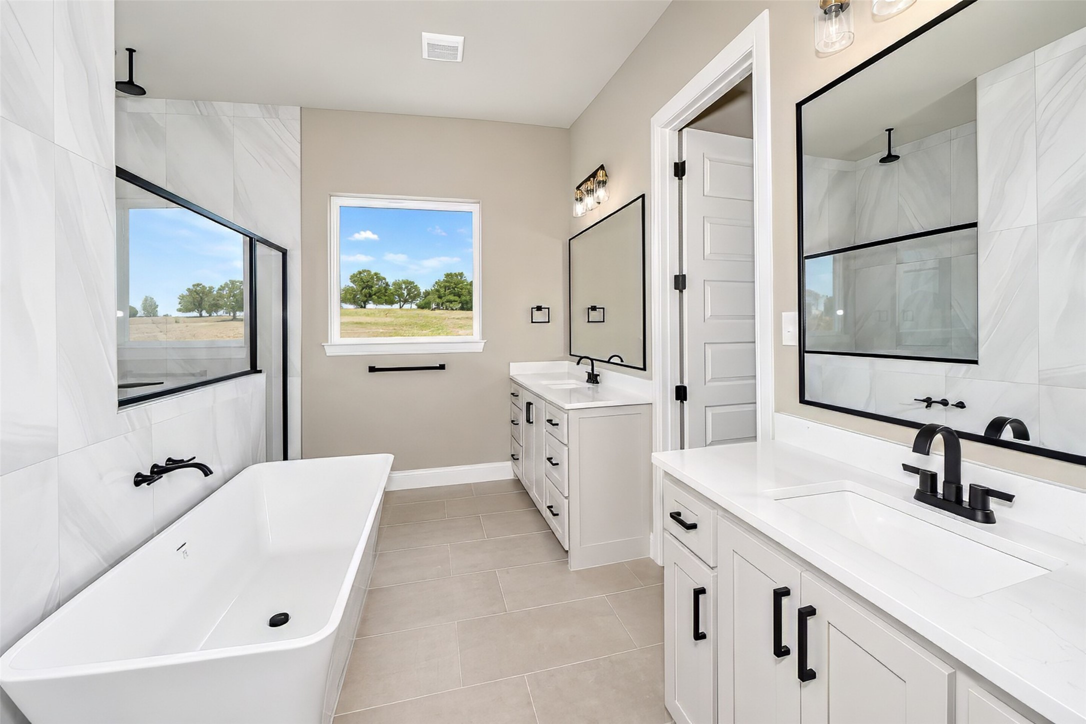 Bathroom with a soaking tub, glass shower, double vanities, and a window overlooking open land.