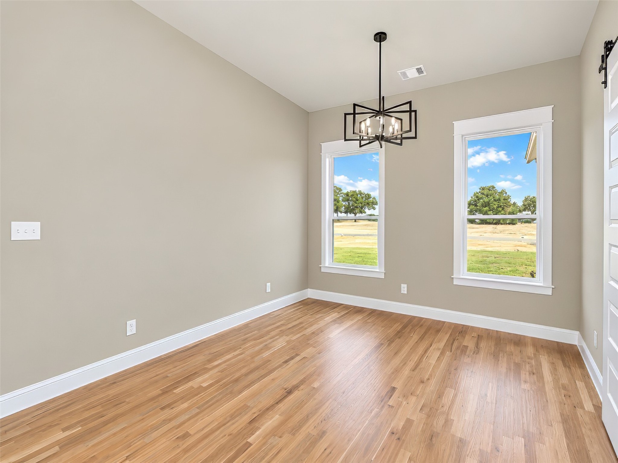 Empty dining room with hardwood floors, two large windows, and a geometric chandelier.