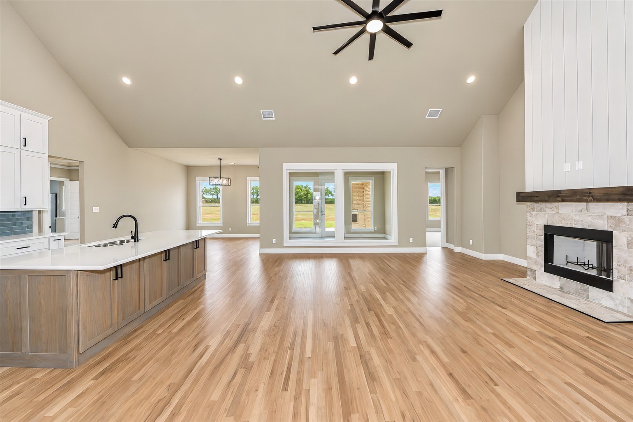 Open-plan kitchen and living area with a wood island, hardwood floors, and a stone fireplace.