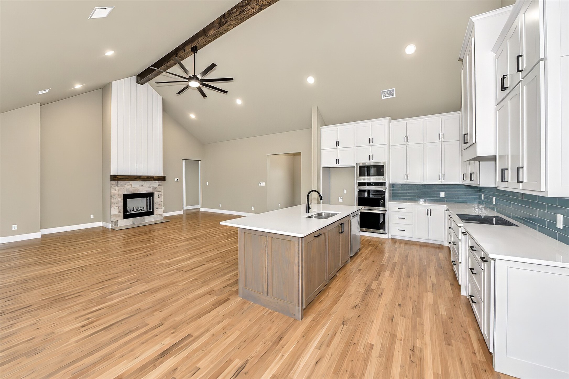 Open-plan kitchen with a large island, white cabinets, hardwood floors, and a stone fireplace.