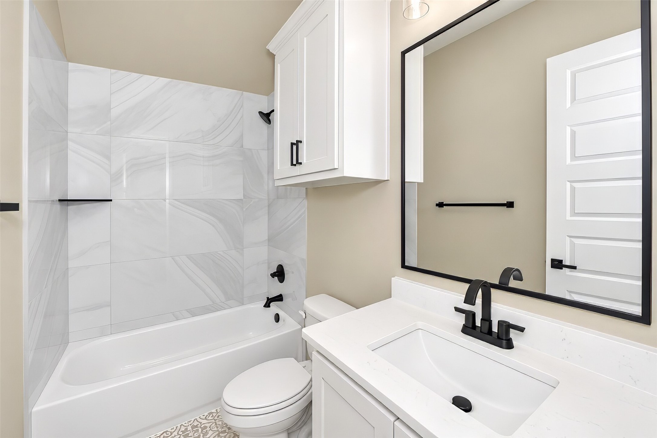 Bathroom with a marble-look tub surround, white vanity, and matte black fixtures.