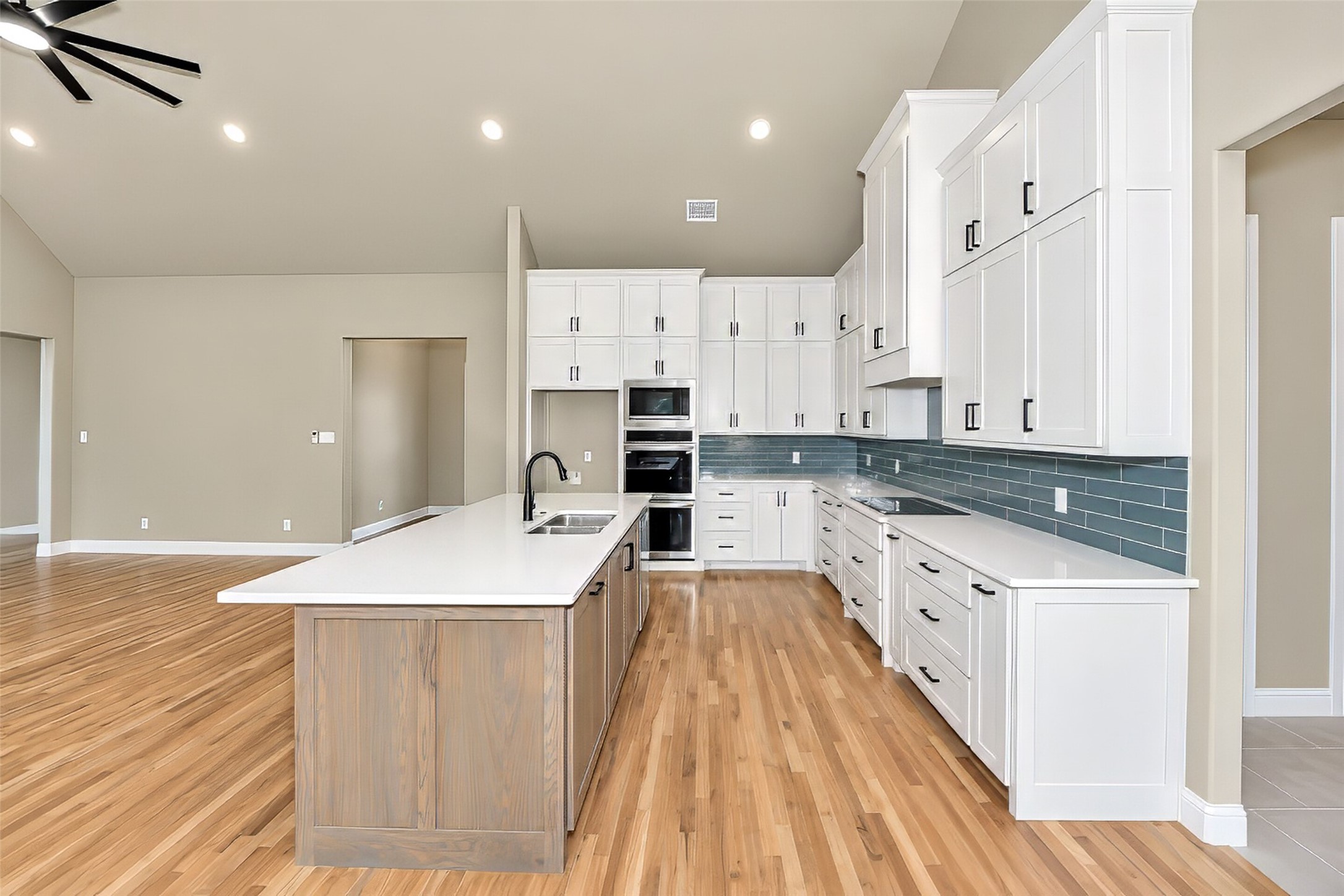 Kitchen with white cabinets, a wood-front island, blue-gray tile backsplash, and hardwood floors.