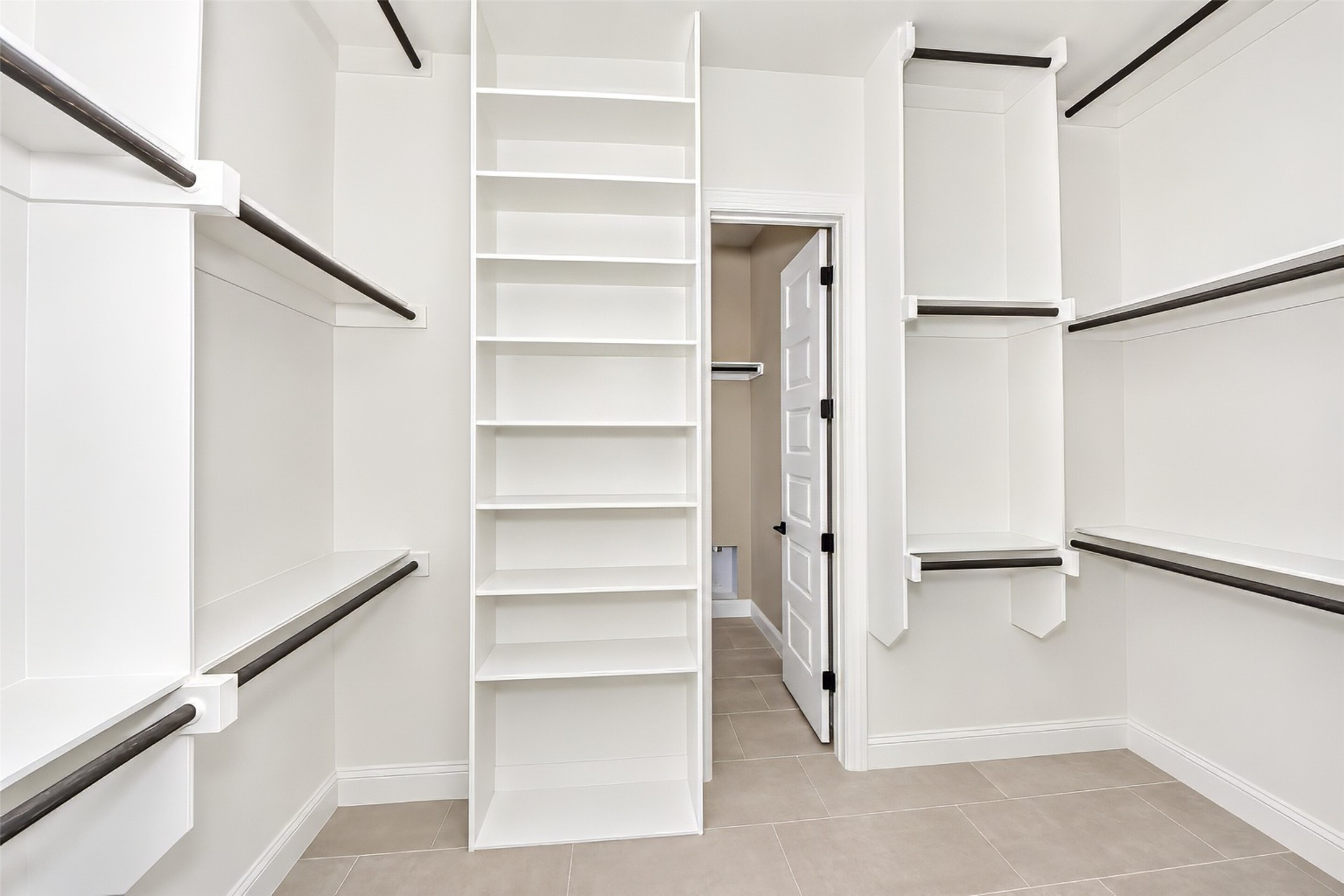 Walk-in closet with white built-in shelves, dark hanging rods, and beige tile flooring.
