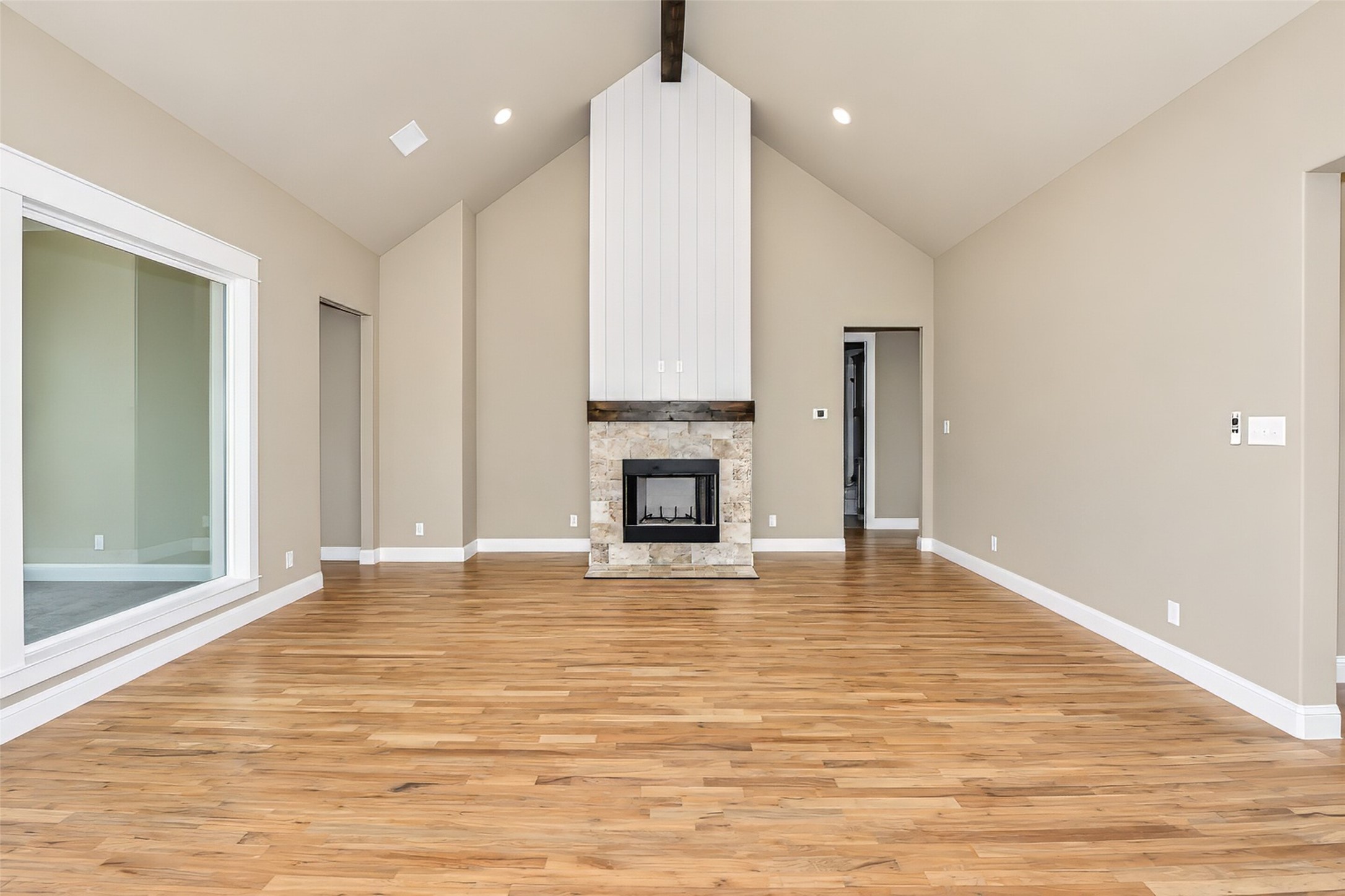 Vacant living room with vaulted ceiling, stone fireplace, and wide-plank wood floors.