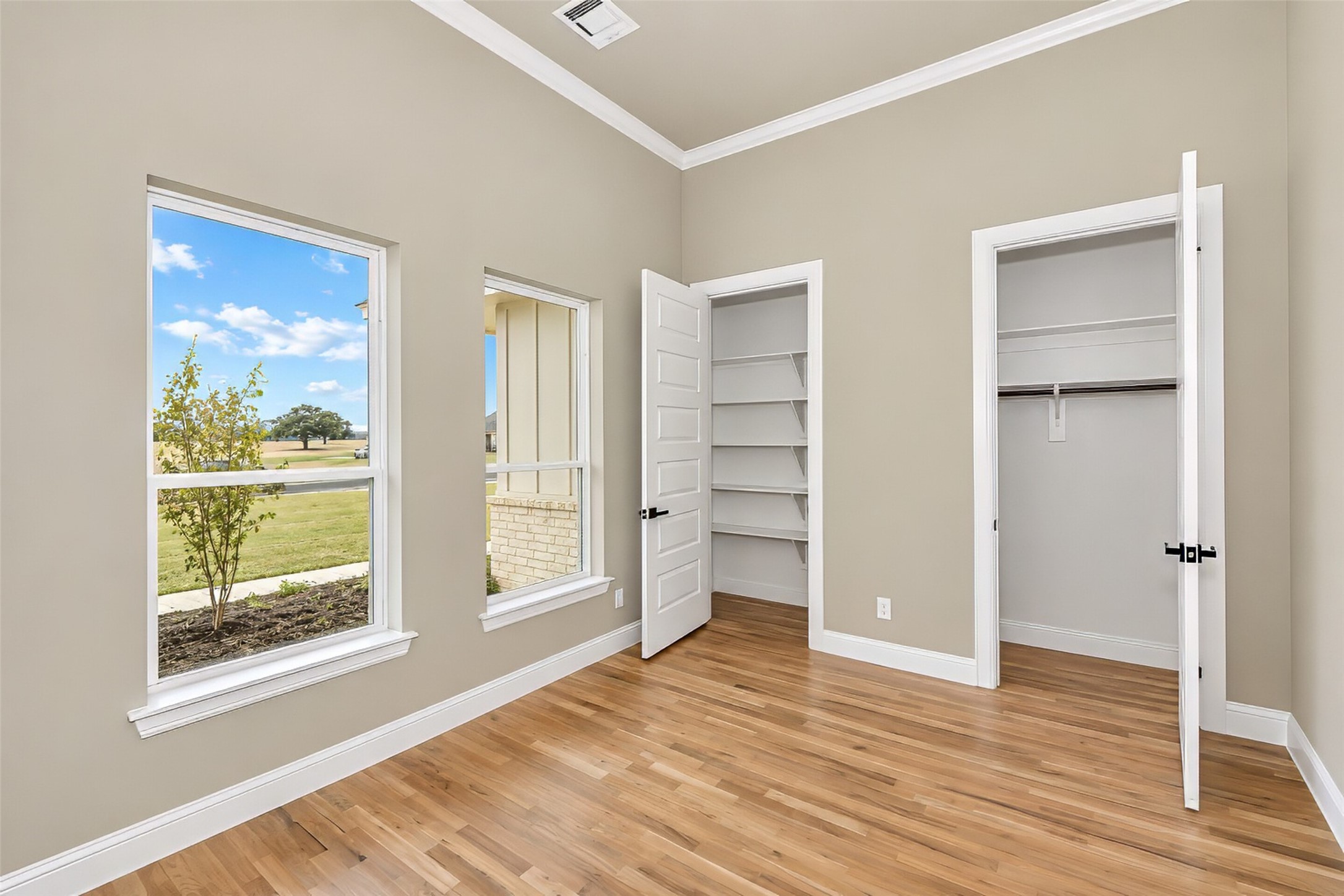 Empty bedroom with hardwood floors, two windows, and two open closets.