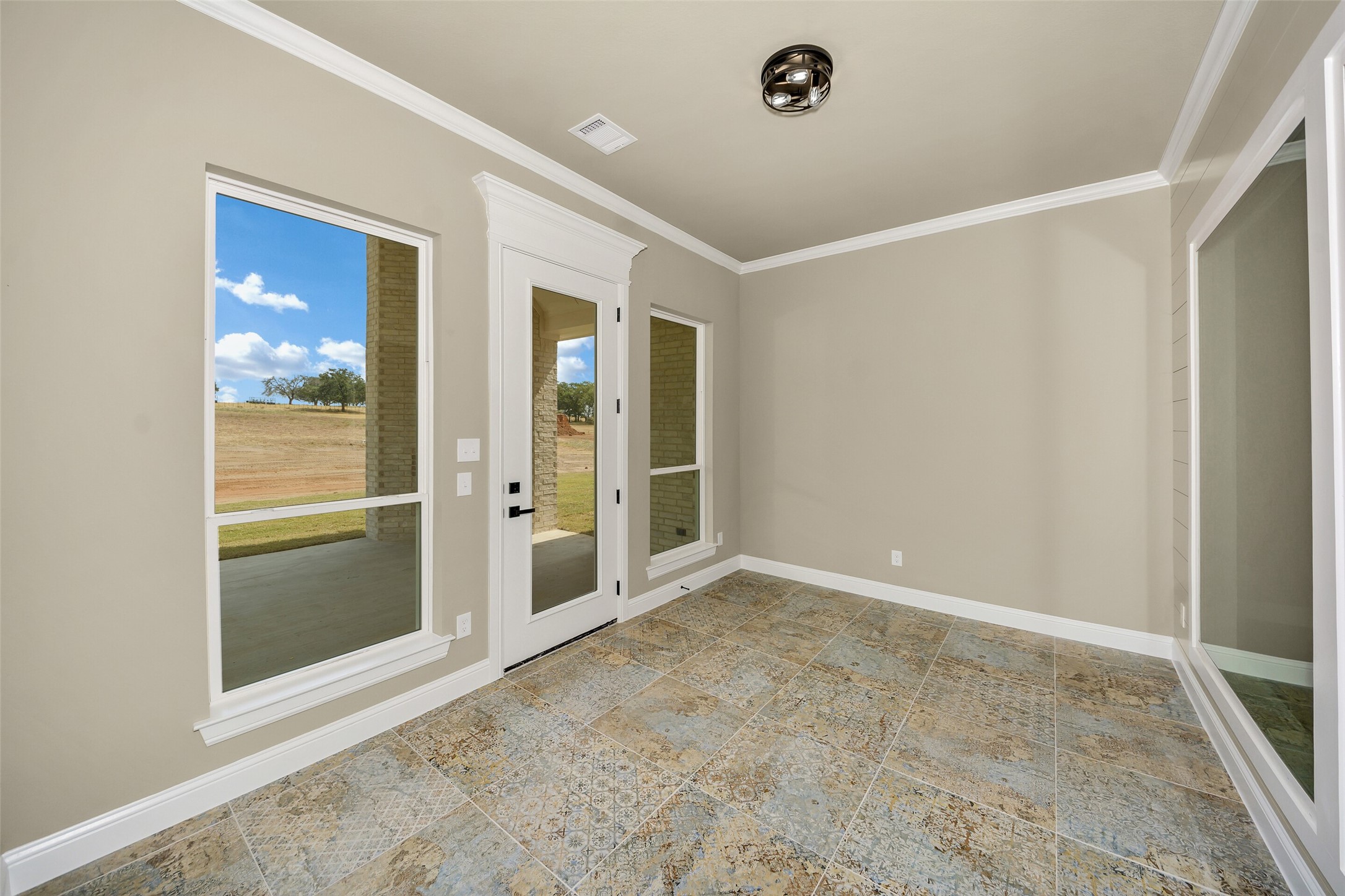 Empty room with patterned tile floors and windows overlooking the yard.