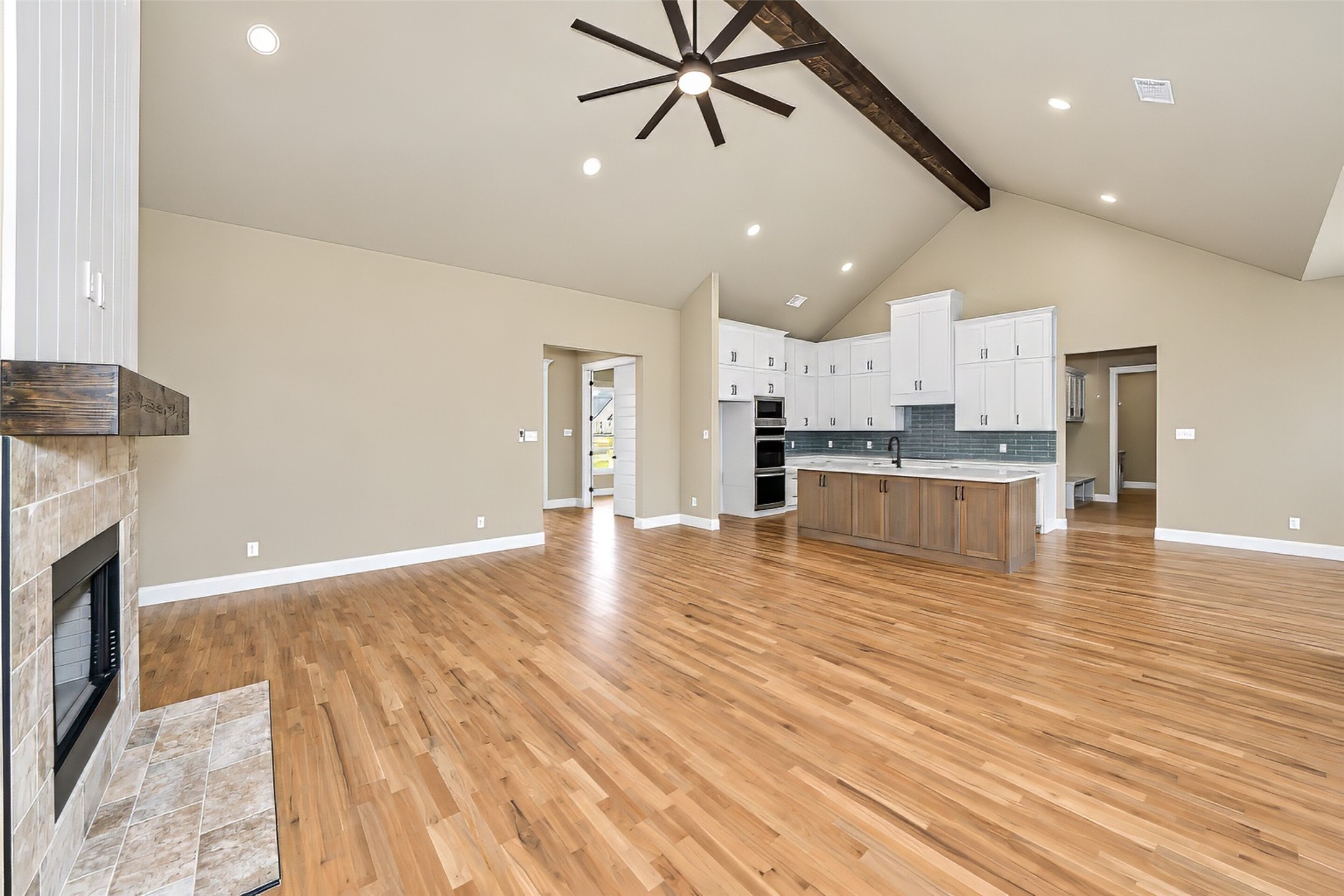 Open-plan living room and kitchen with hardwood floors, stone fireplace, and vaulted ceiling.