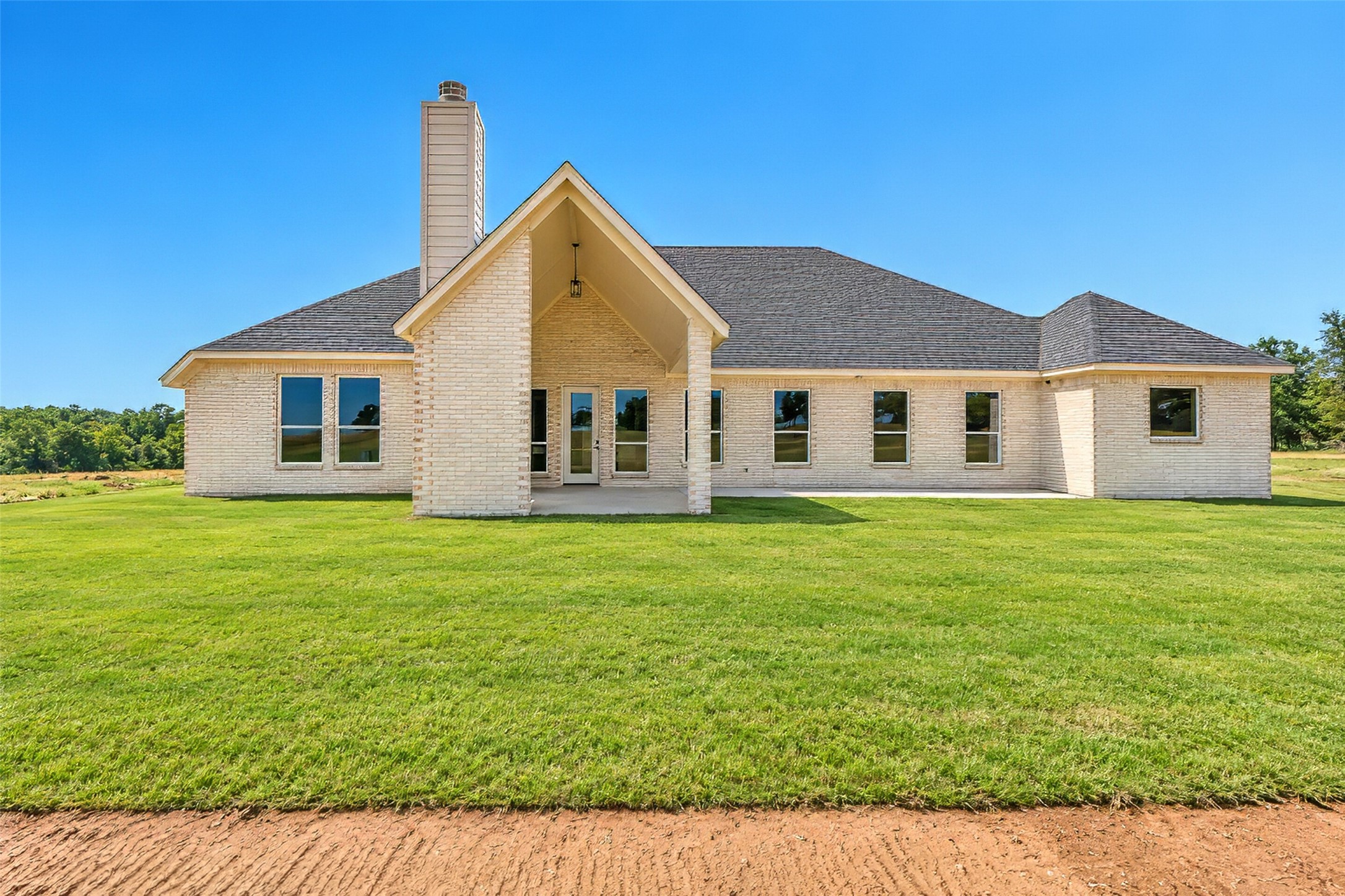 Rear view of a light brick home with a tall gabled porch and chimney, set behind a broad green lawn.