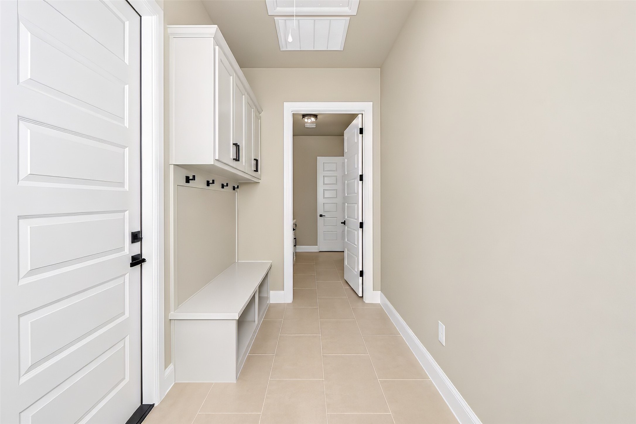 Mudroom hallway with white built-in cabinets, coat hooks, a bench, and beige tile flooring.