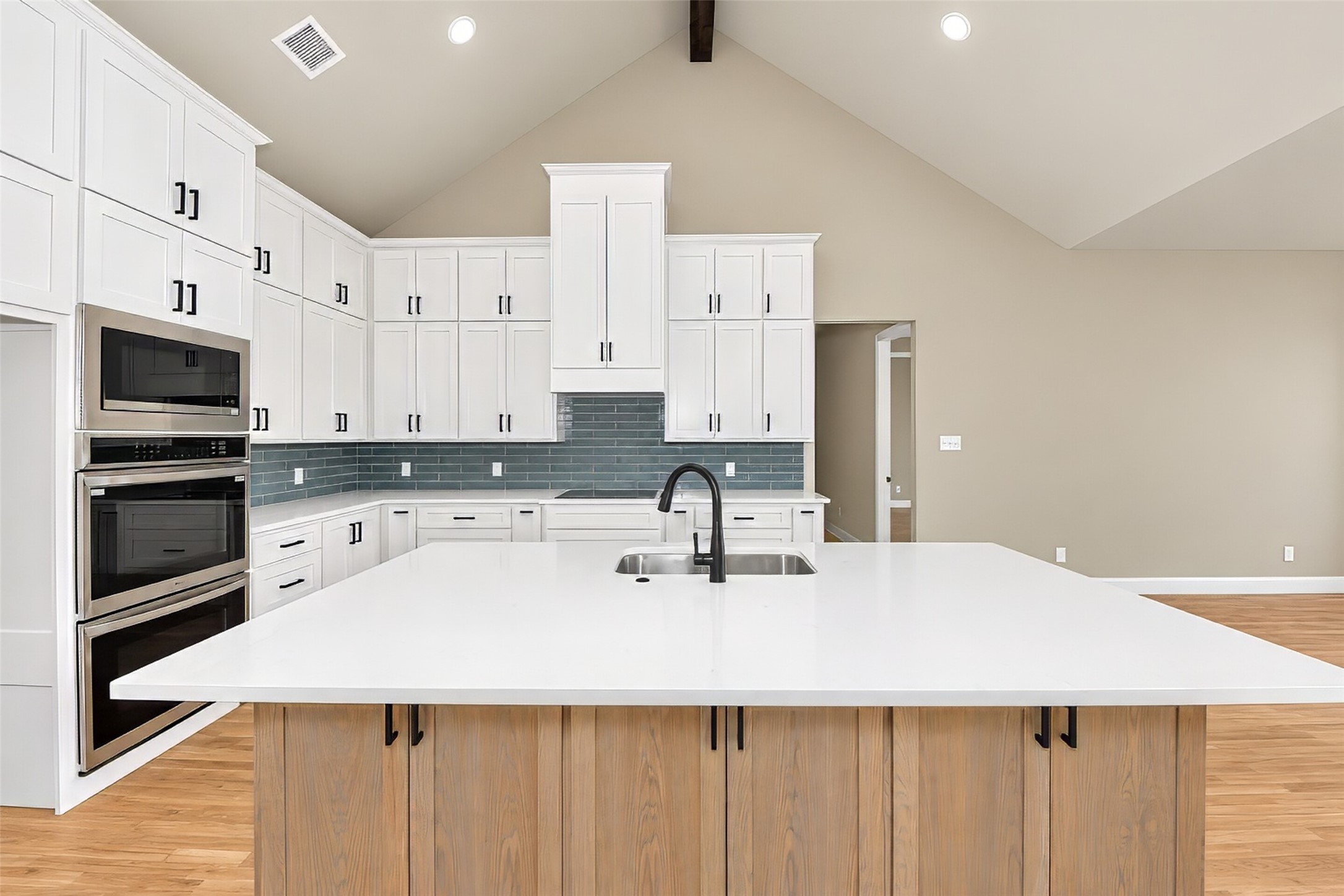 Kitchen with a large white island, dark faucet, white cabinets, and stainless steel double ovens.